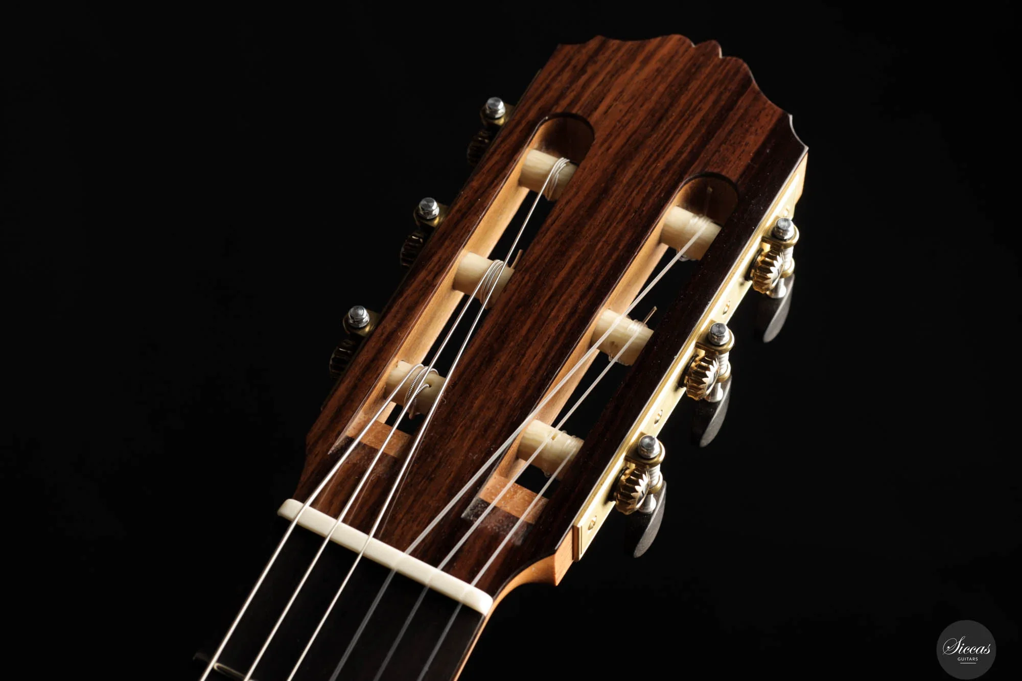 Close-up of a classical guitar headstock with tuning pegs, strings, and nut against a black background.