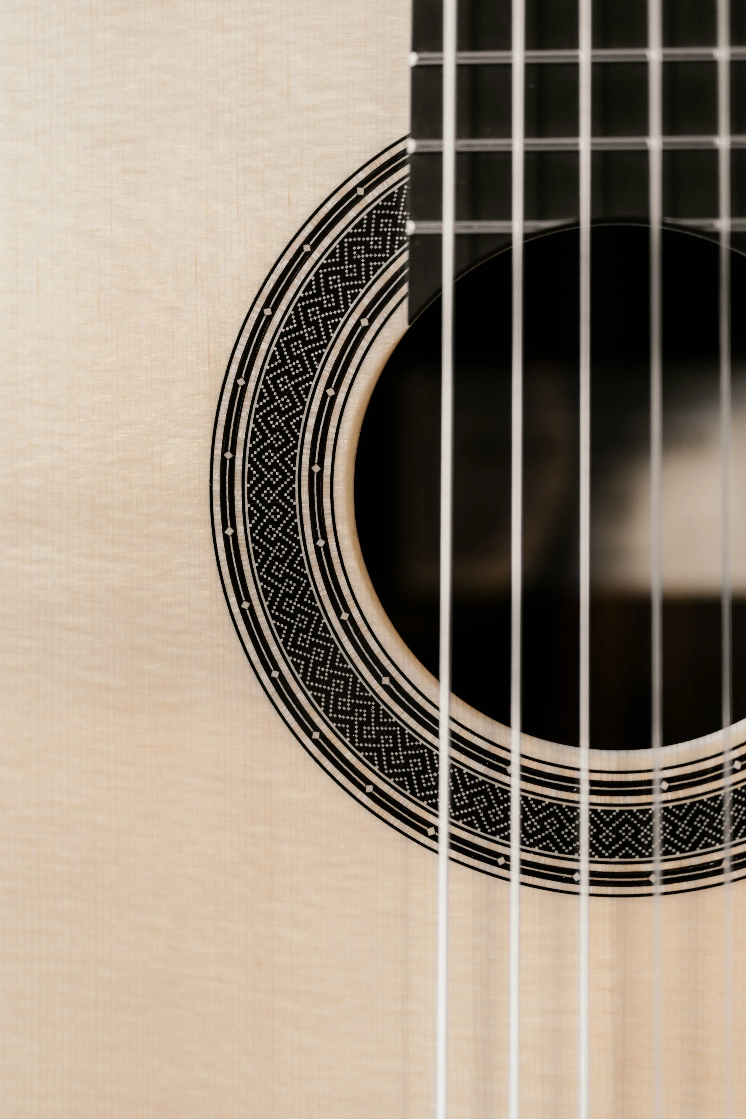 Close-up of an acoustic guitar with a light wood body, black decorative rosette around the sound hole, and strings visible.