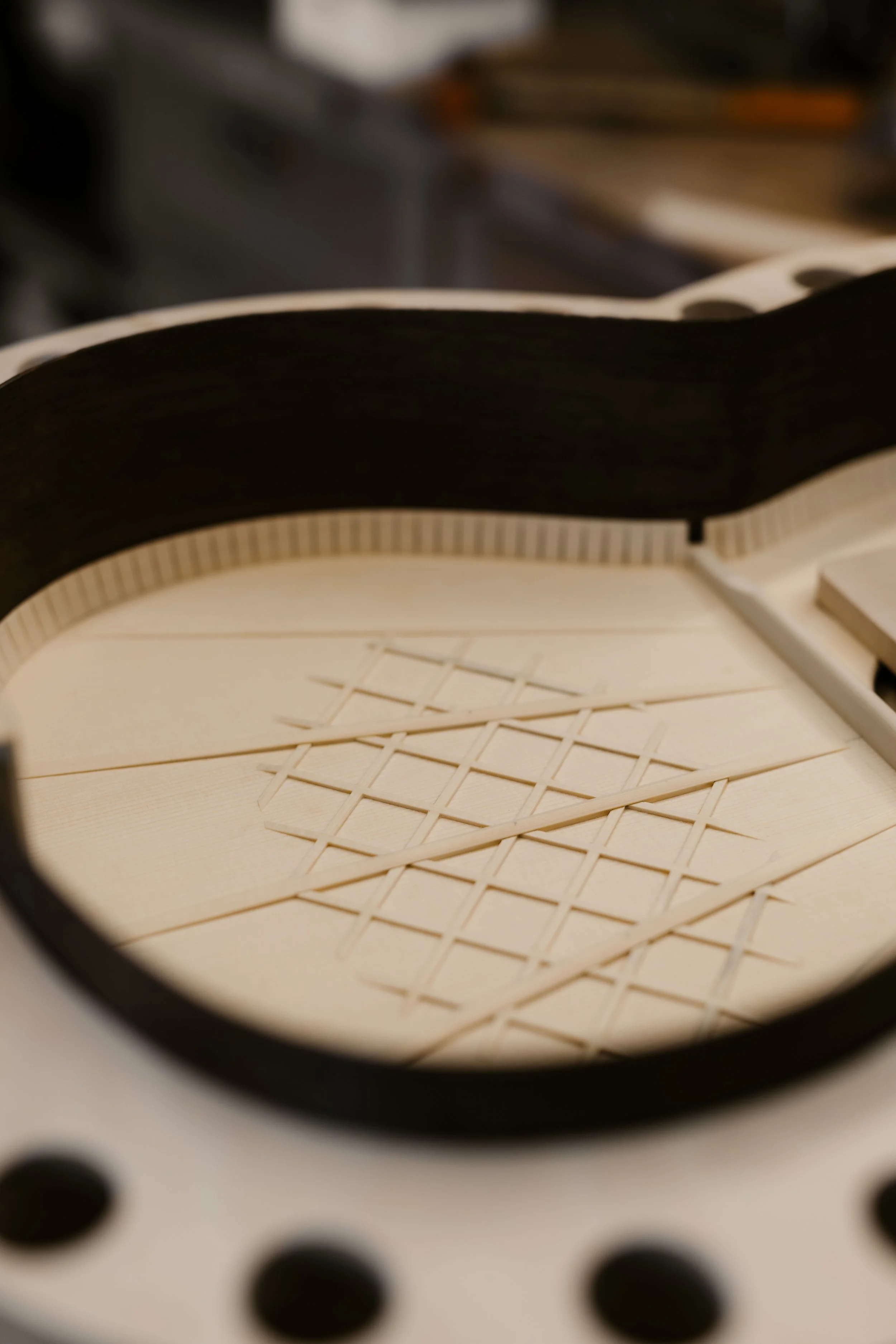 Close-up of a partially built wooden classical guitar inside its drum-shaped body, with the fretboard and strings not yet attached.