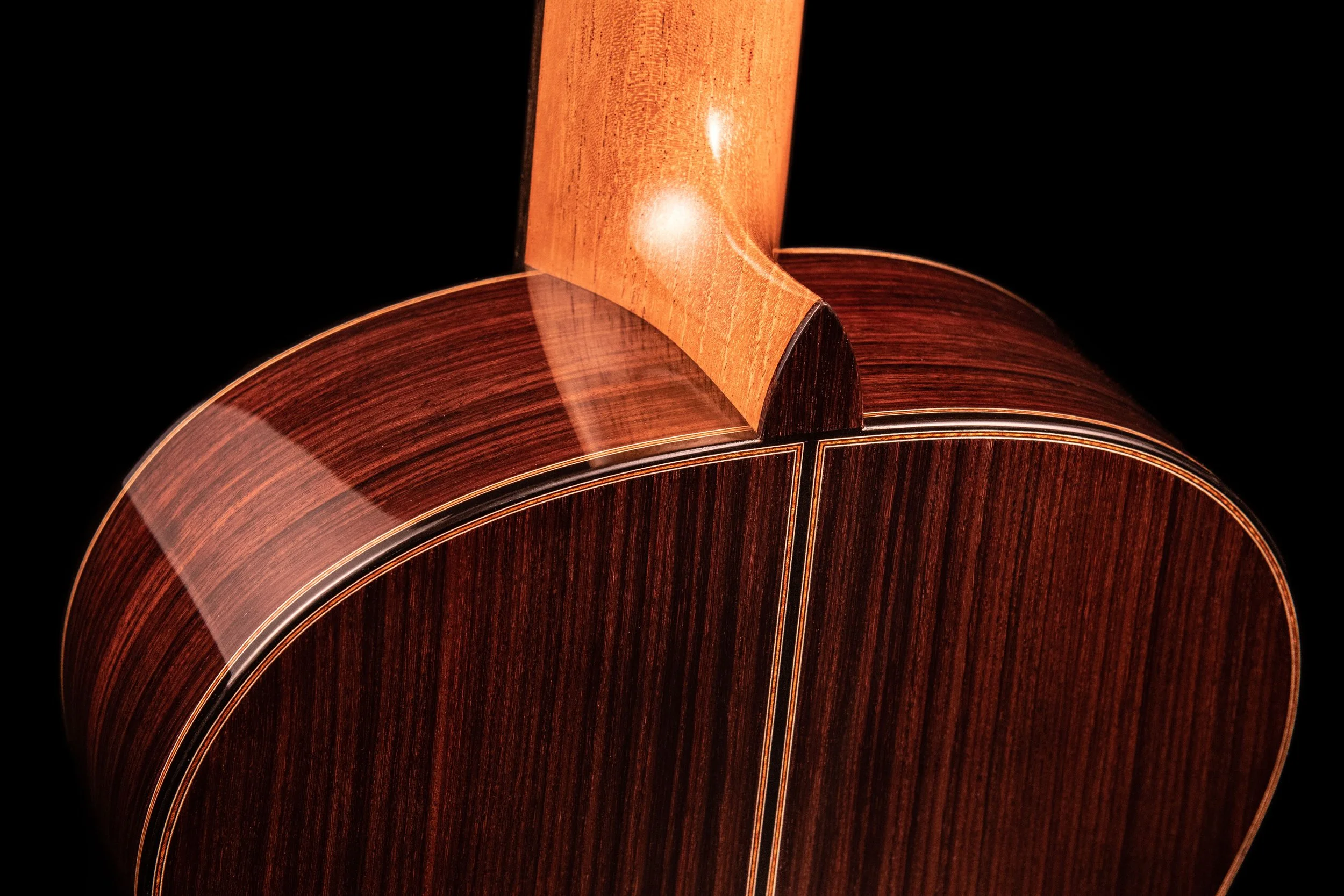 Close-up of the back of an acoustic guitar showing the wooden grain and detailed craftsmanship.