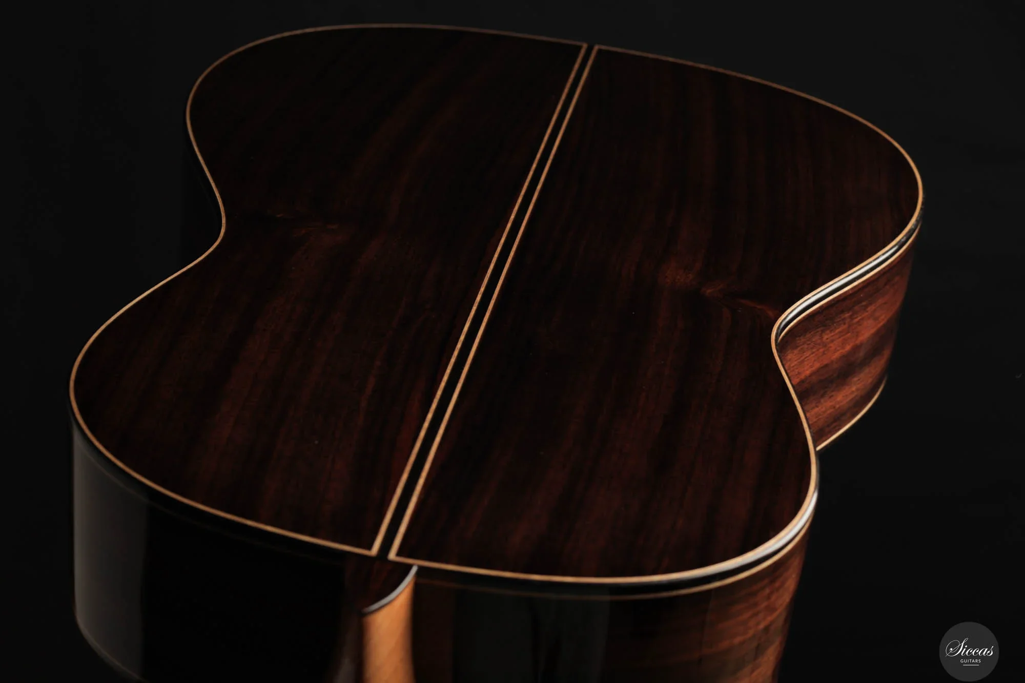 Close-up of the back of a dark wood acoustic guitar with light binding, set against a black background.