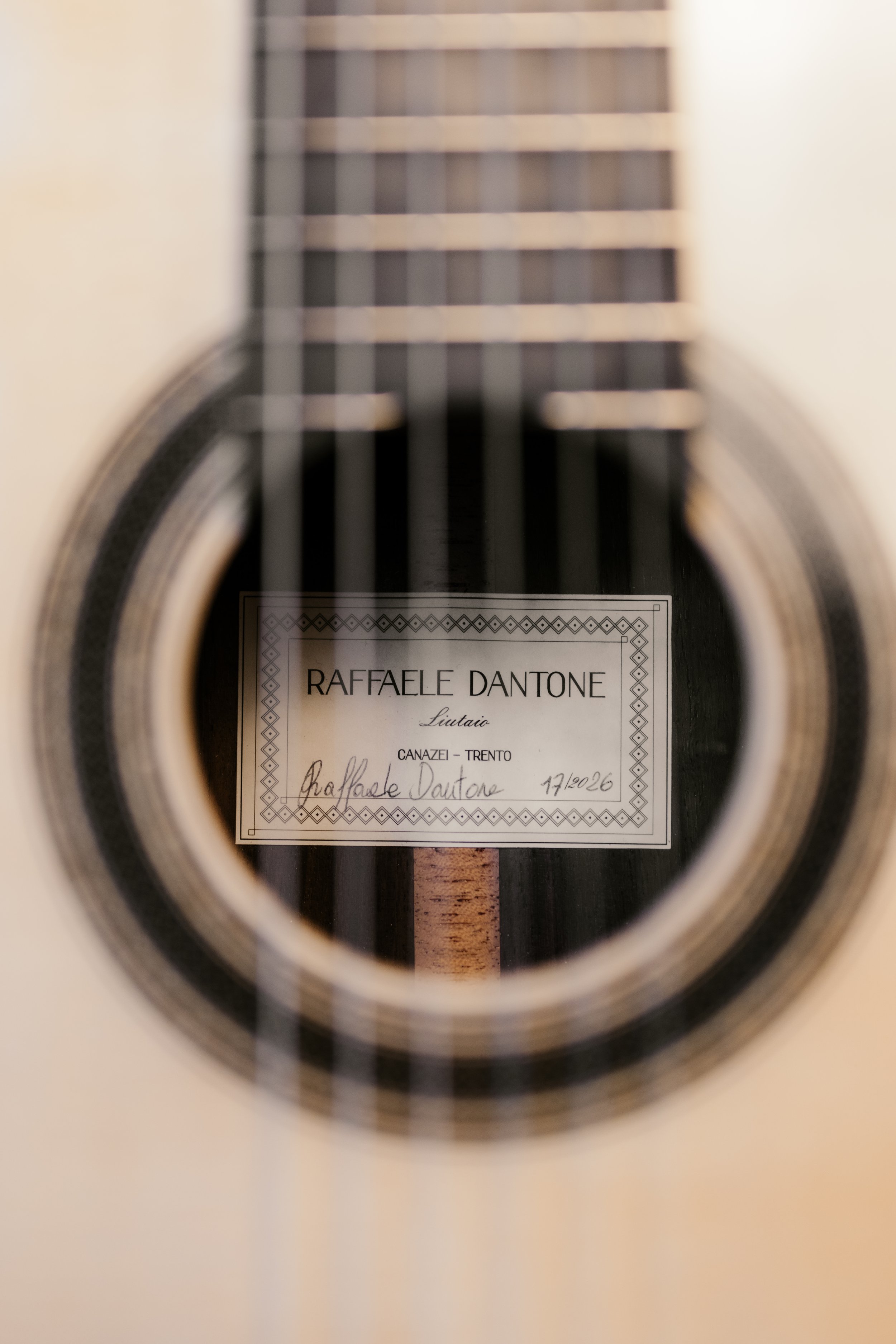 Close-up view inside the sound hole of an acoustic guitar, showing a label with the name 'Raffaele Dantone', hand-written details, and string bridge.