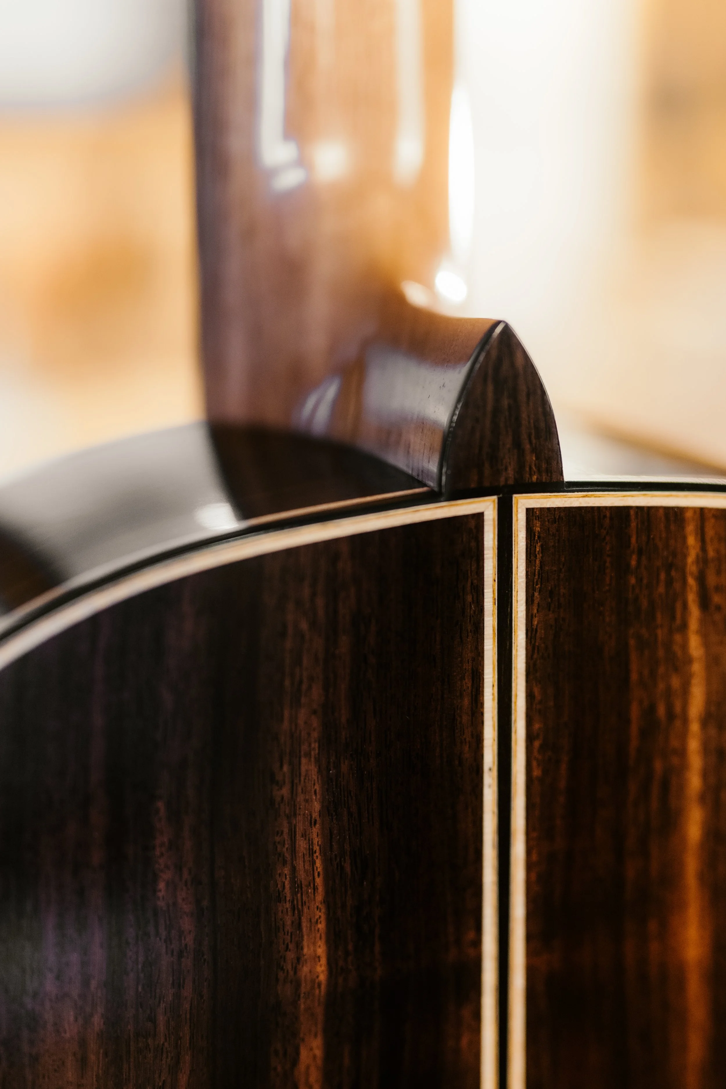 Close-up of an acoustic guitar's body and neck, focusing on the dark wood finish and decorative binding.