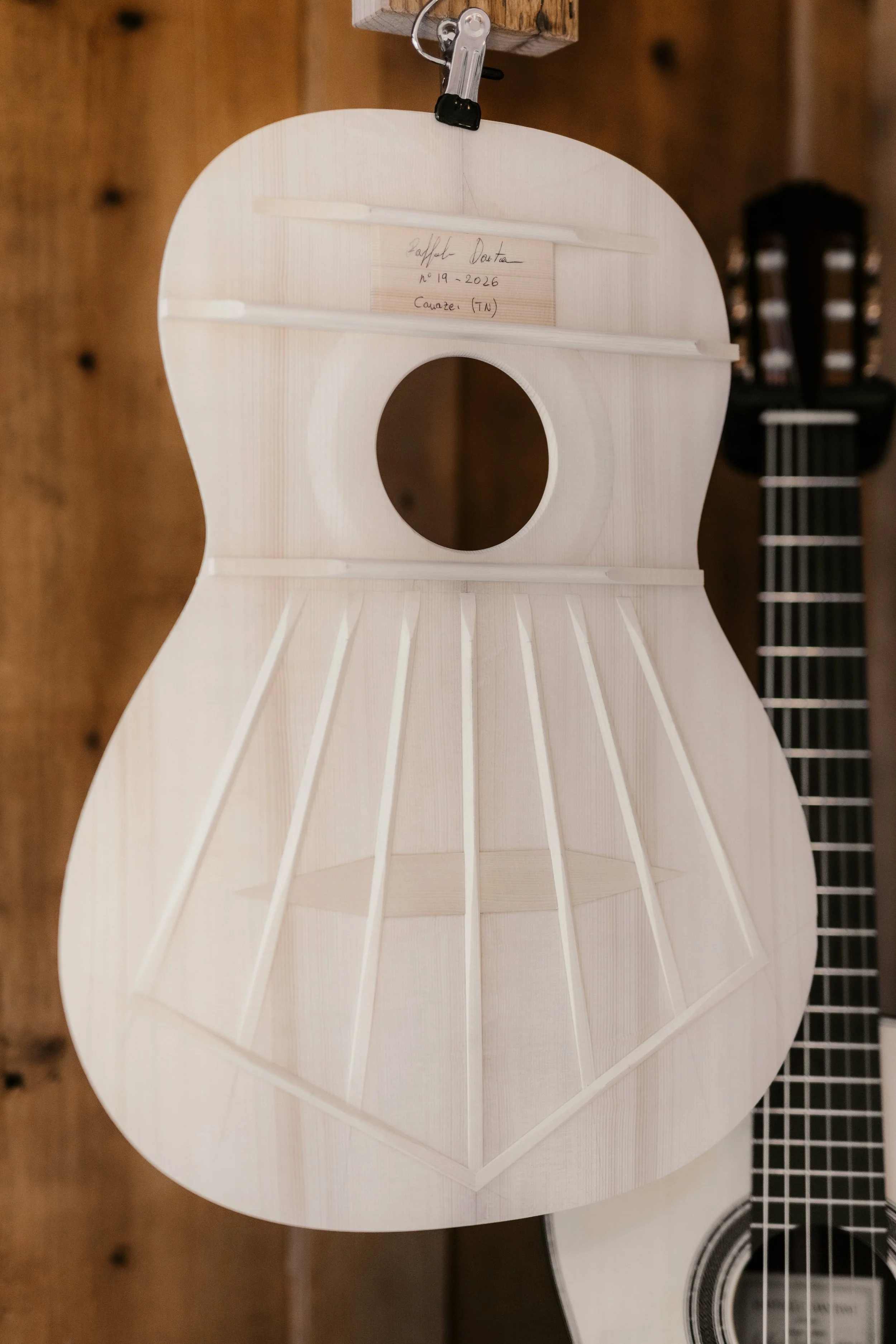 Unfinished wooden guitar body hanging on a wall in a workshop.