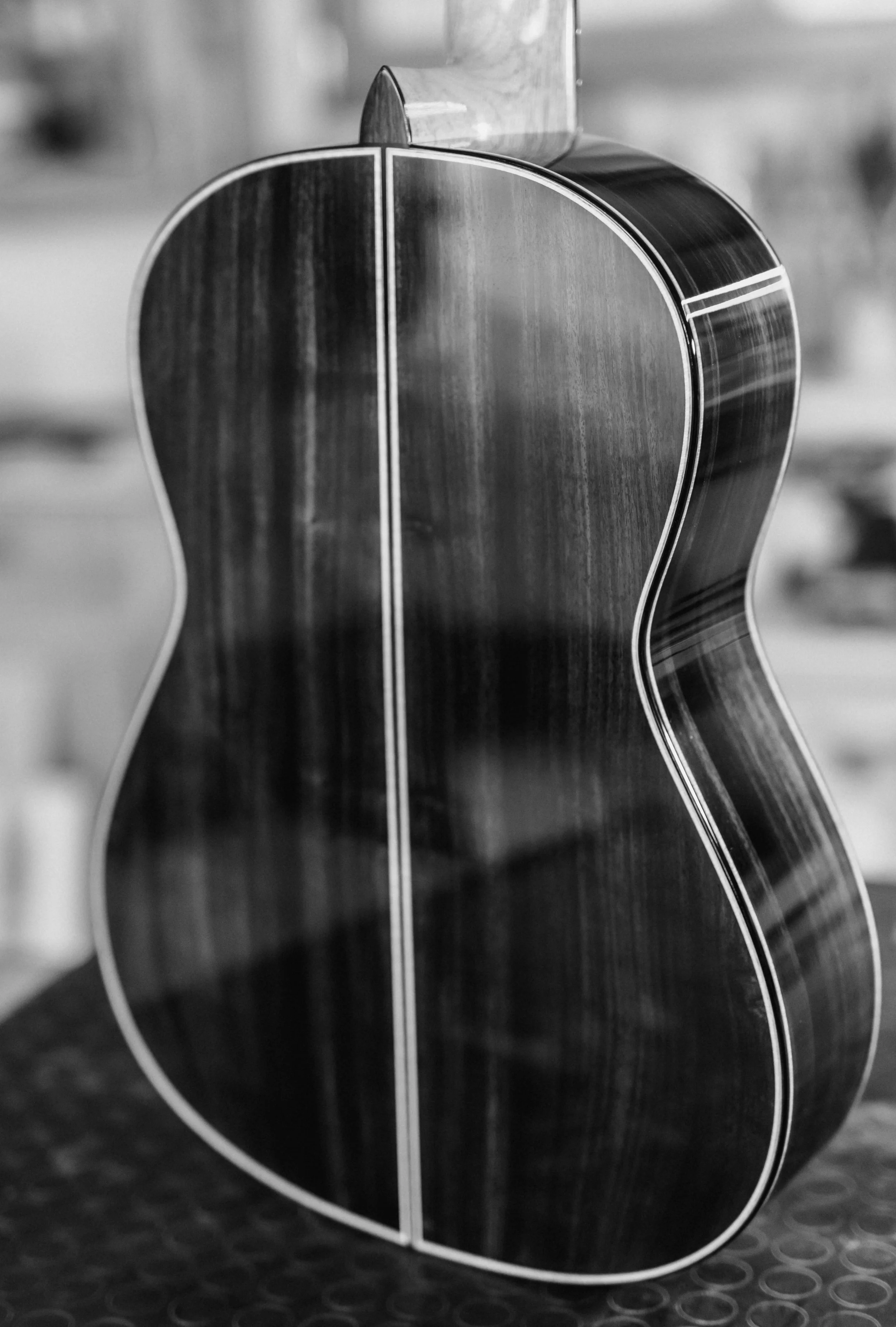 Close-up black and white photo of an classical guitar's back and side, showing polished wood grain and binding detail.