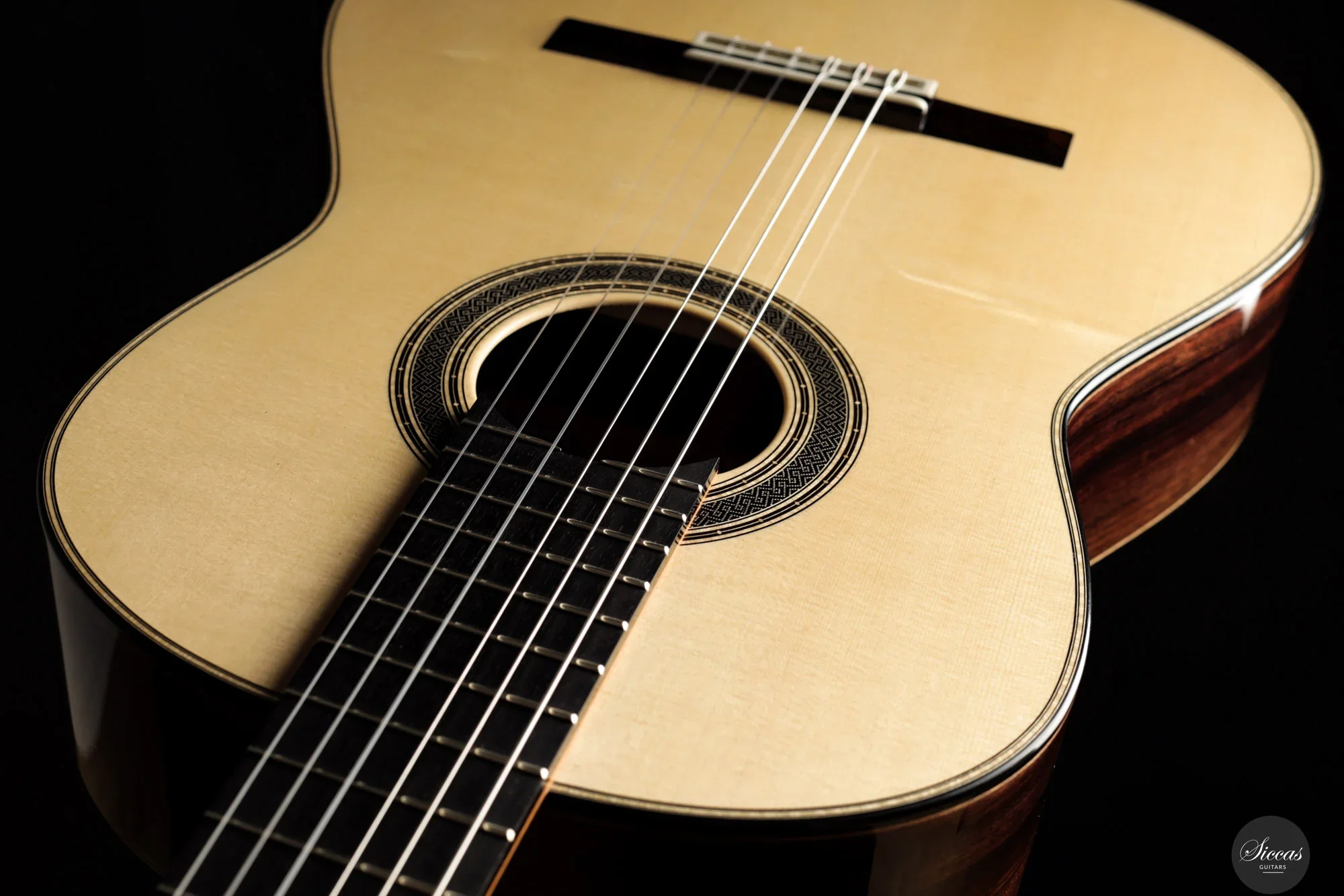 Close-up of an classical guitar with a natural wood finish, showing the strings, sound hole, and part of the body against a black background.