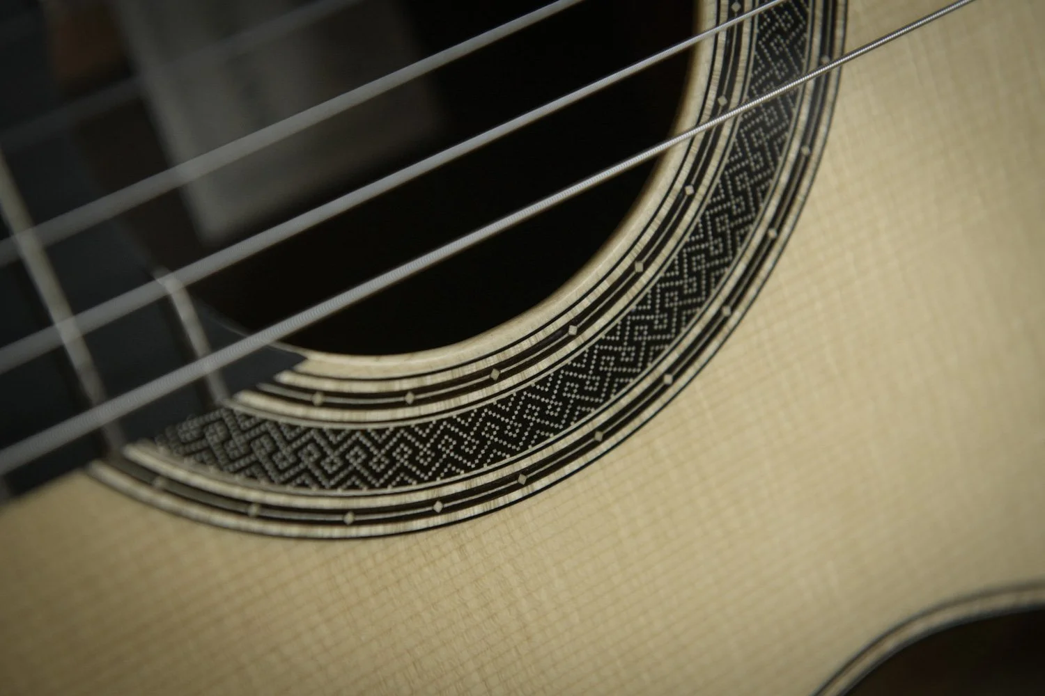 Close-up of an acoustic guitar's sound hole and decorative rosette with intricate geometric patterns.