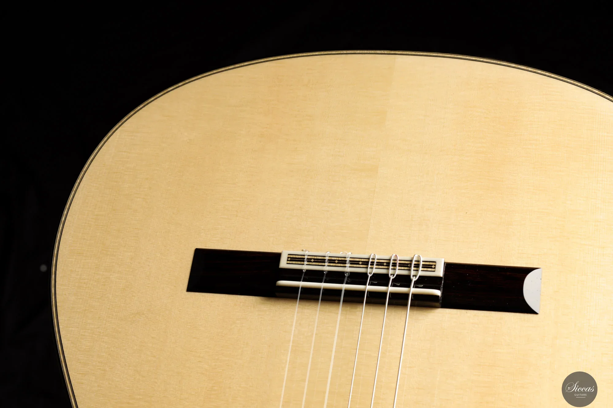 Close-up of a classical guitar's soundhole, strings, and bridge against a black background.
