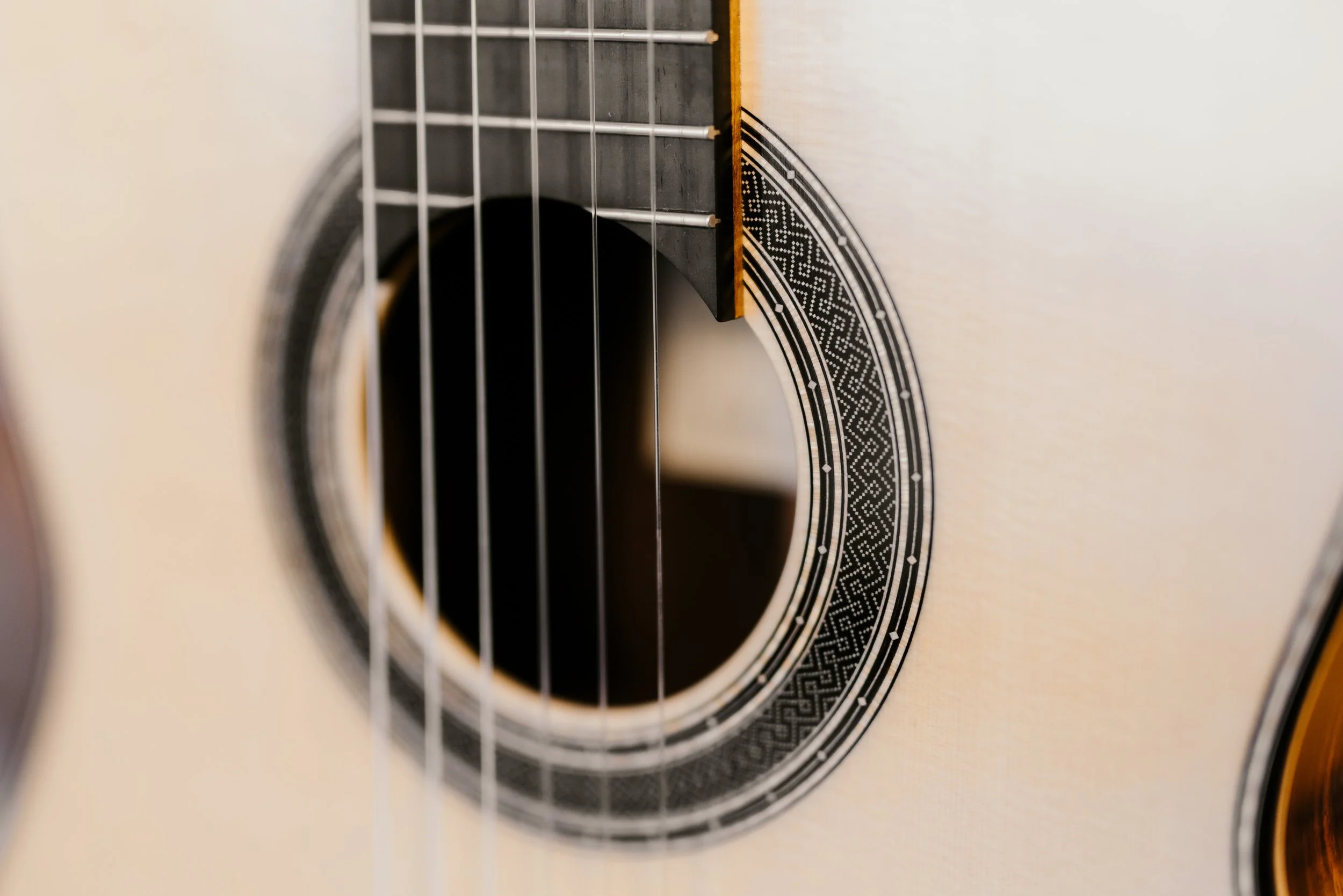 Close-up of an acoustic guitar's sound hole with intricate black and white rosette design, strings, and part of the fretboard visible.