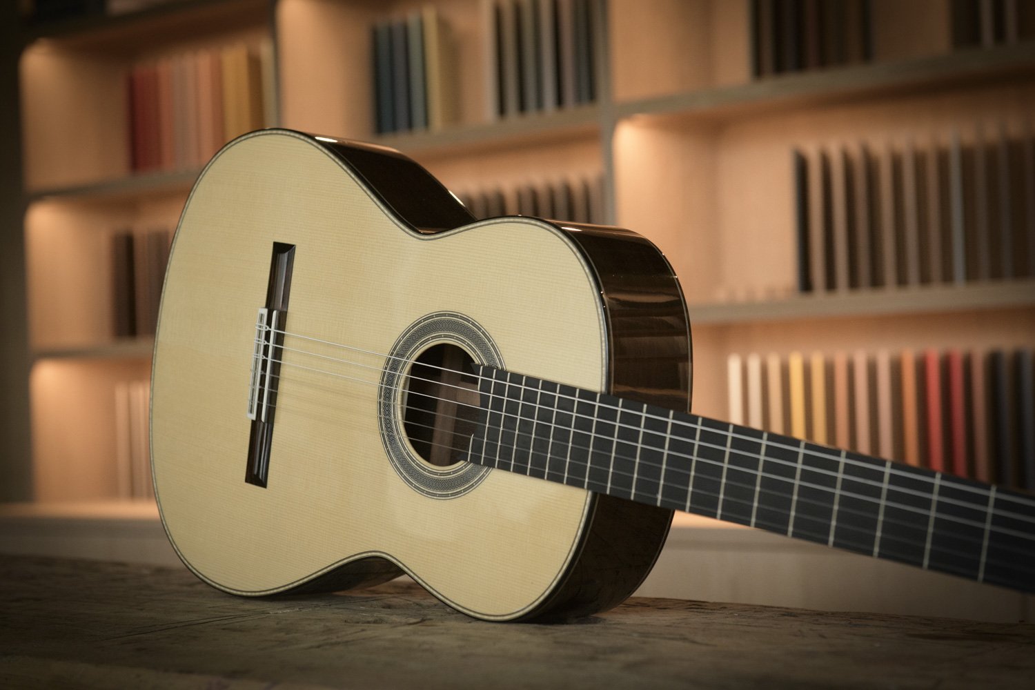 An acoustic guitar lying on a wooden surface with a backdrop of bookshelves filled with books.