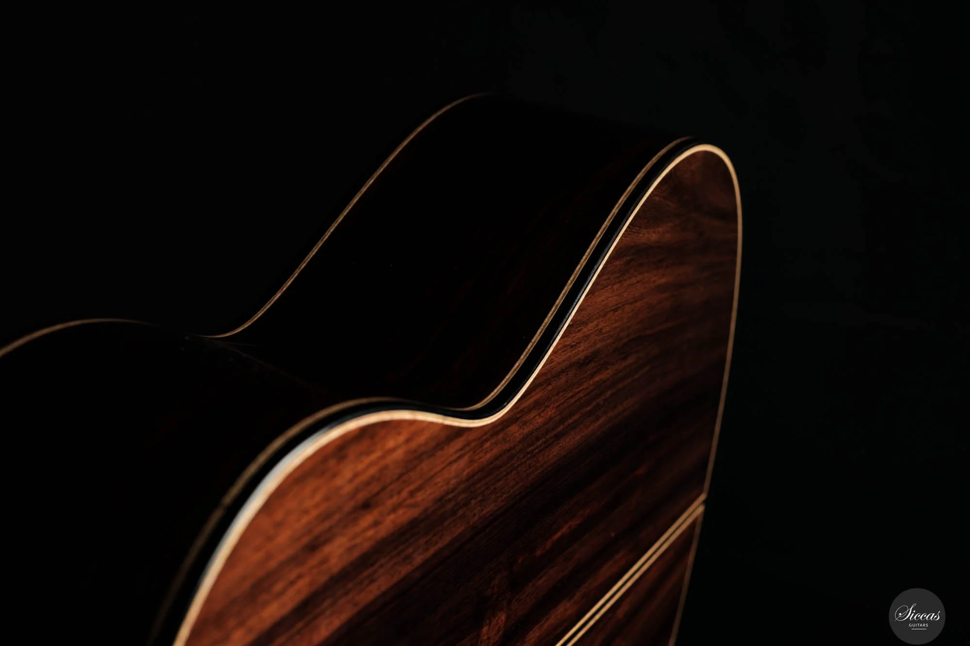 Close-up of a wooden acoustic guitar against a black background, highlighting its dark wood grain and smooth curved shape with light-colored binding.