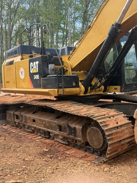Yellow Caterpillar 349E excavator on dirt ground with track system, trees in background.