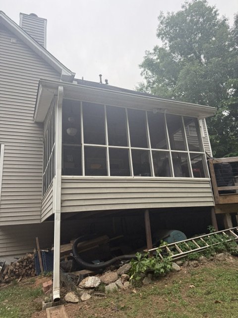 A house with a screened-in porch or sunroom extension at the back. The porch is elevated, with support beams underneath, and has large windows.