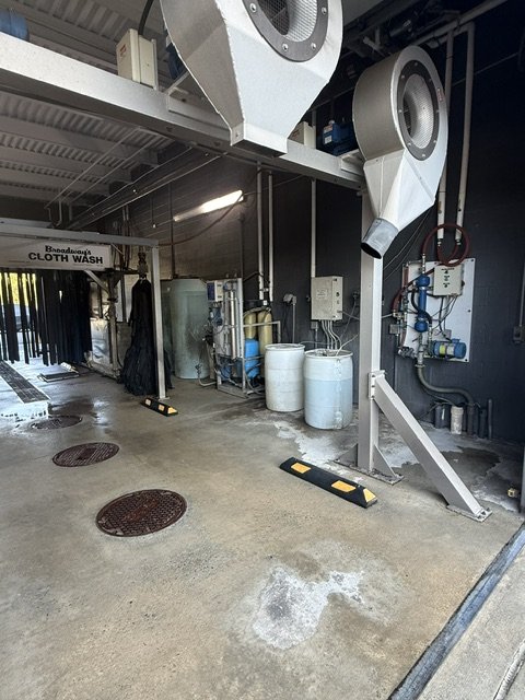 Industrial laundry facility with drying machines, carts, and laundry supplies.