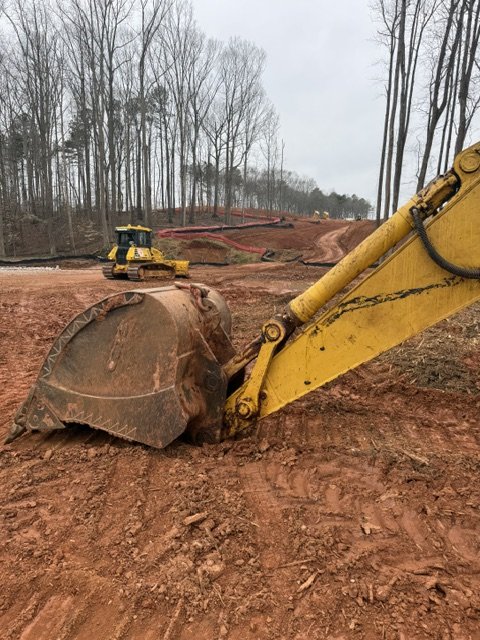 Construction site with an excavator digging into the dirt and a bulldozer in the background.