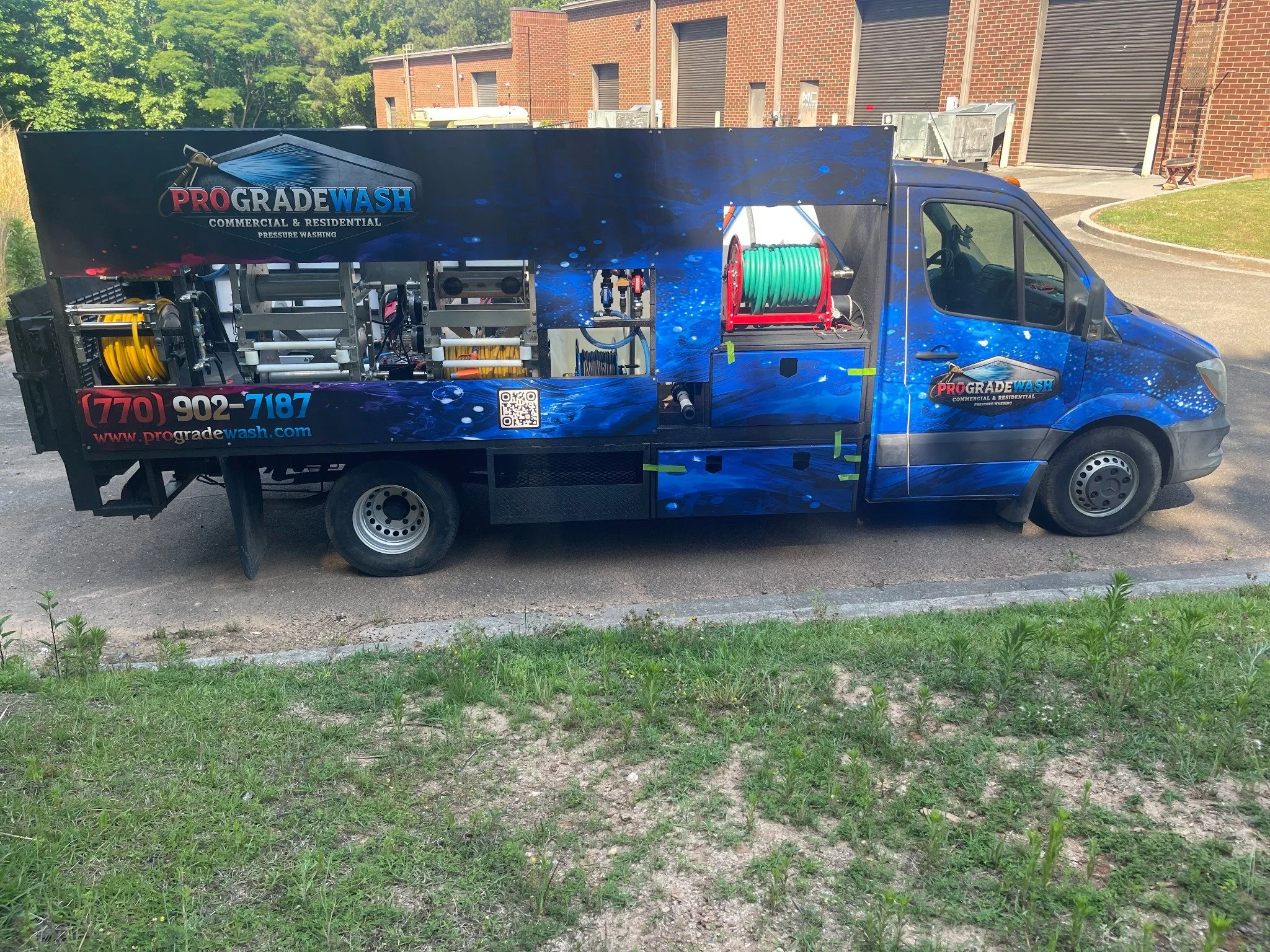 Blue ProGrade Wash service truck with hoses and cleaning equipment outside a brick building