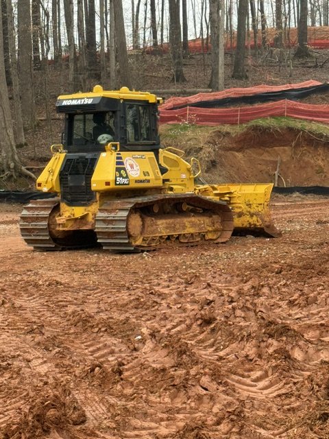 Yellow bulldozer on a construction site with dirt and trees in the background.