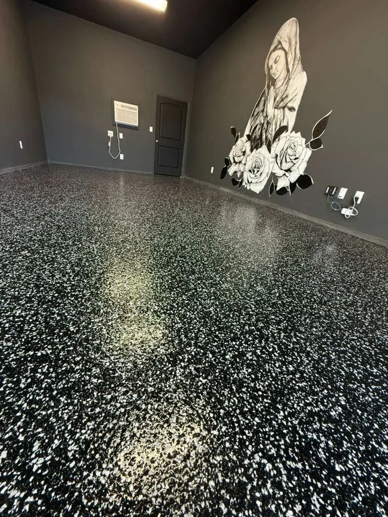 Empty room with black and white speckled floor, dark gray walls, wall art of a woman with roses, and a closed gray door.