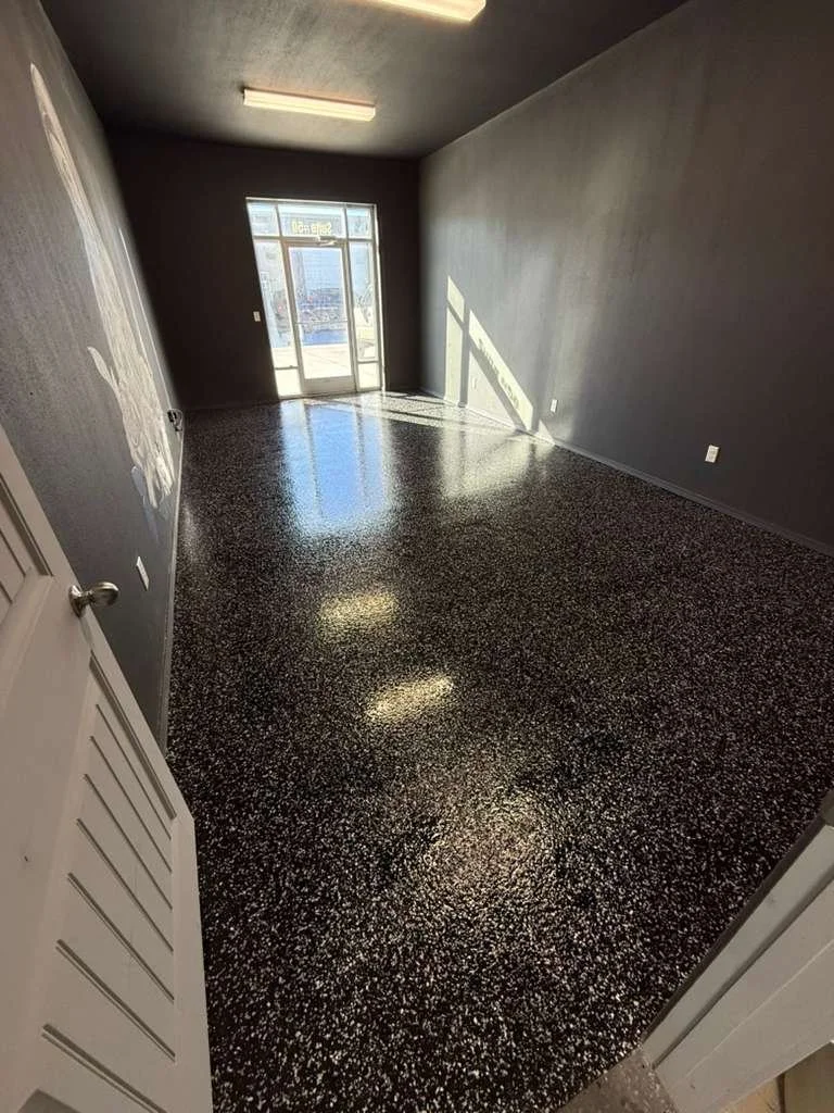 Empty room with gray walls, a door with glass panels, terrazzo flooring, and sunlight streaming in through the door.