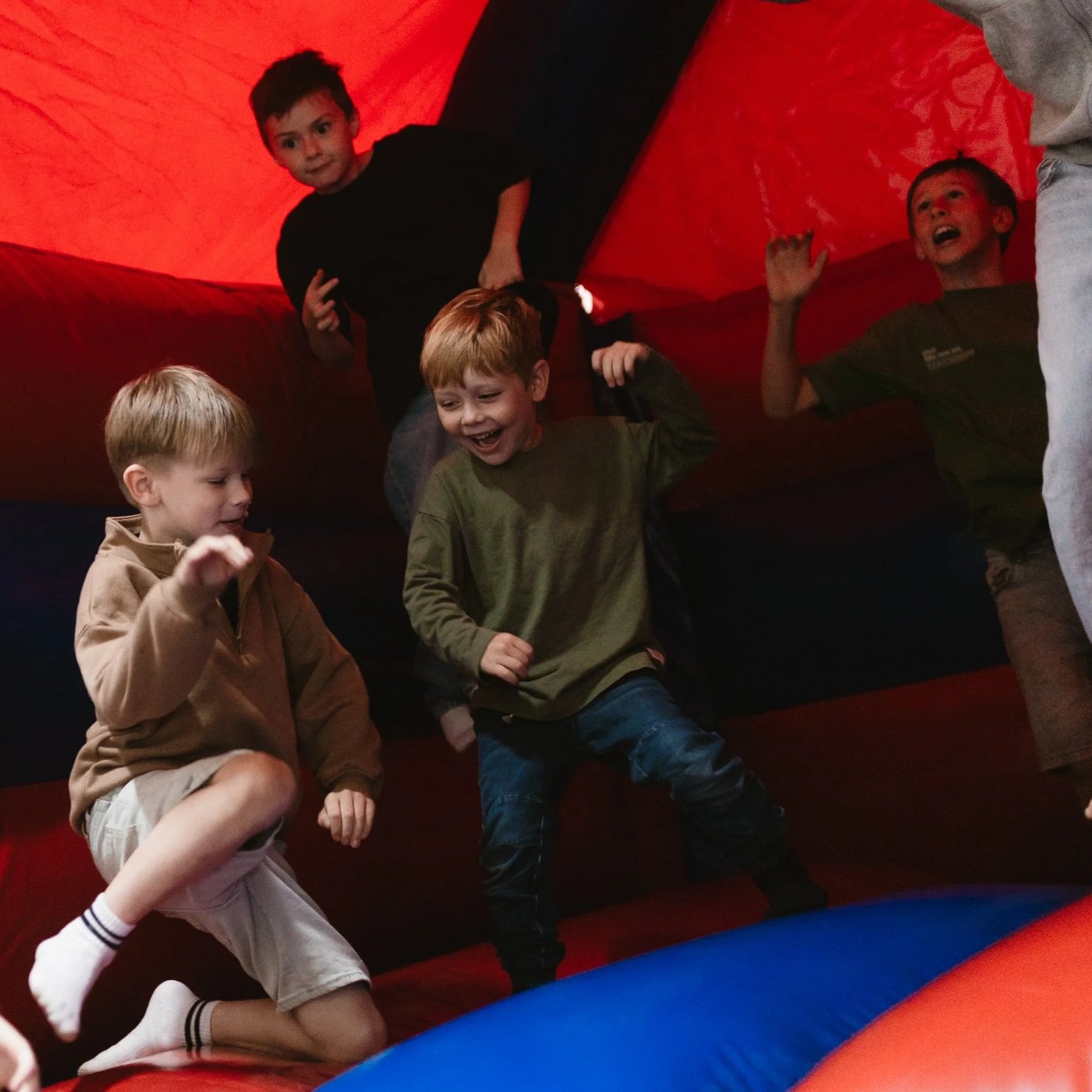 Group of children playing inside an inflatable bounce house, with red walls and a blue and orange floor.