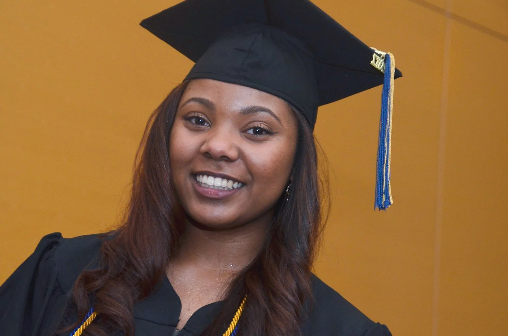 A young woman in a graduation cap and gown smiling for a photo.