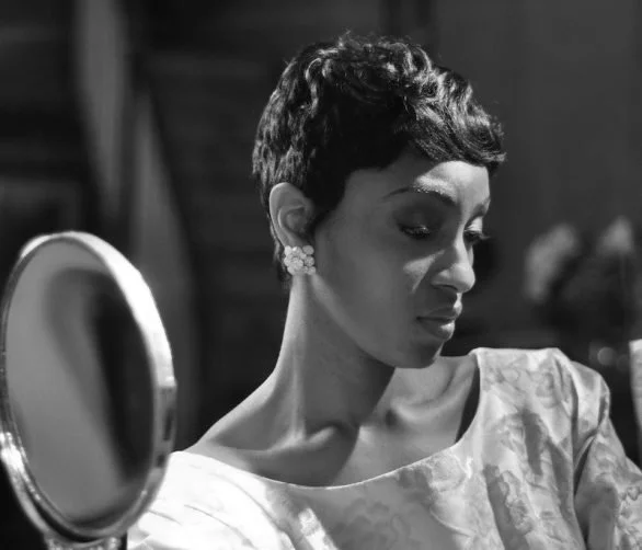 A woman with short dark hair and earrings, looking into a mirror, in a black and white photo.