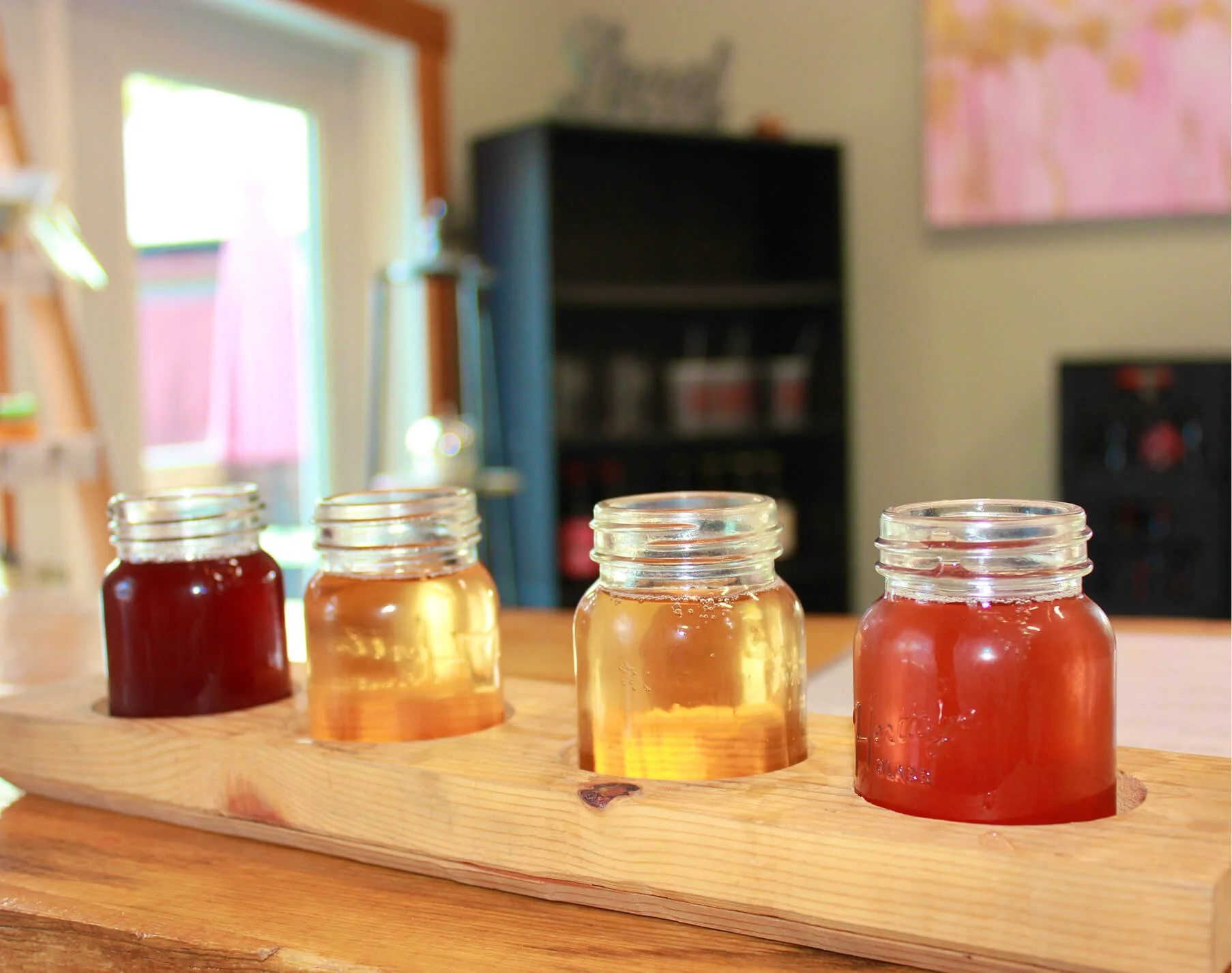 Four glass jars filled with different types of hard cider displayed on a wooden board.