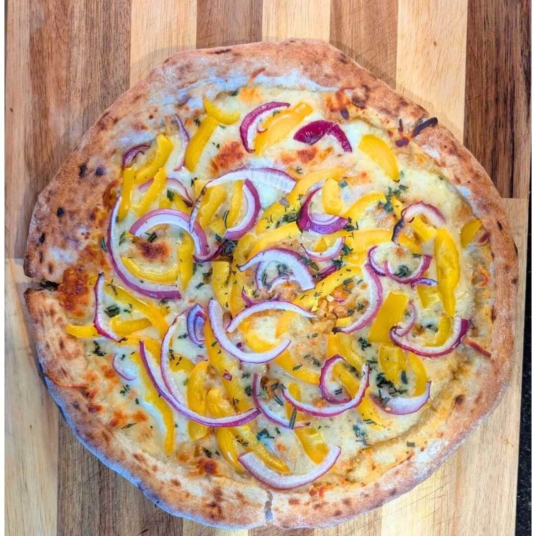 A pizza with a golden brown crust topped with melted cheese, sliced red onions, and yellow bell peppers on a wooden surface.