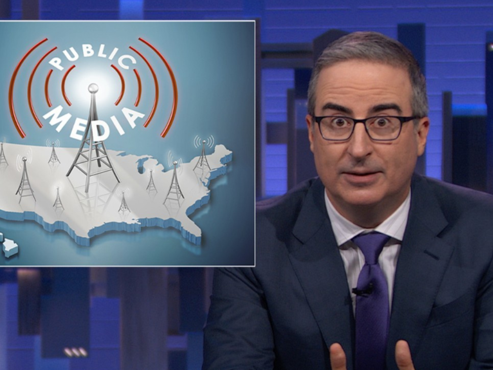 Television host sitting at desk with a graphic of the United States map and radio towers labeled 'Public Media' on a screen behind him.
