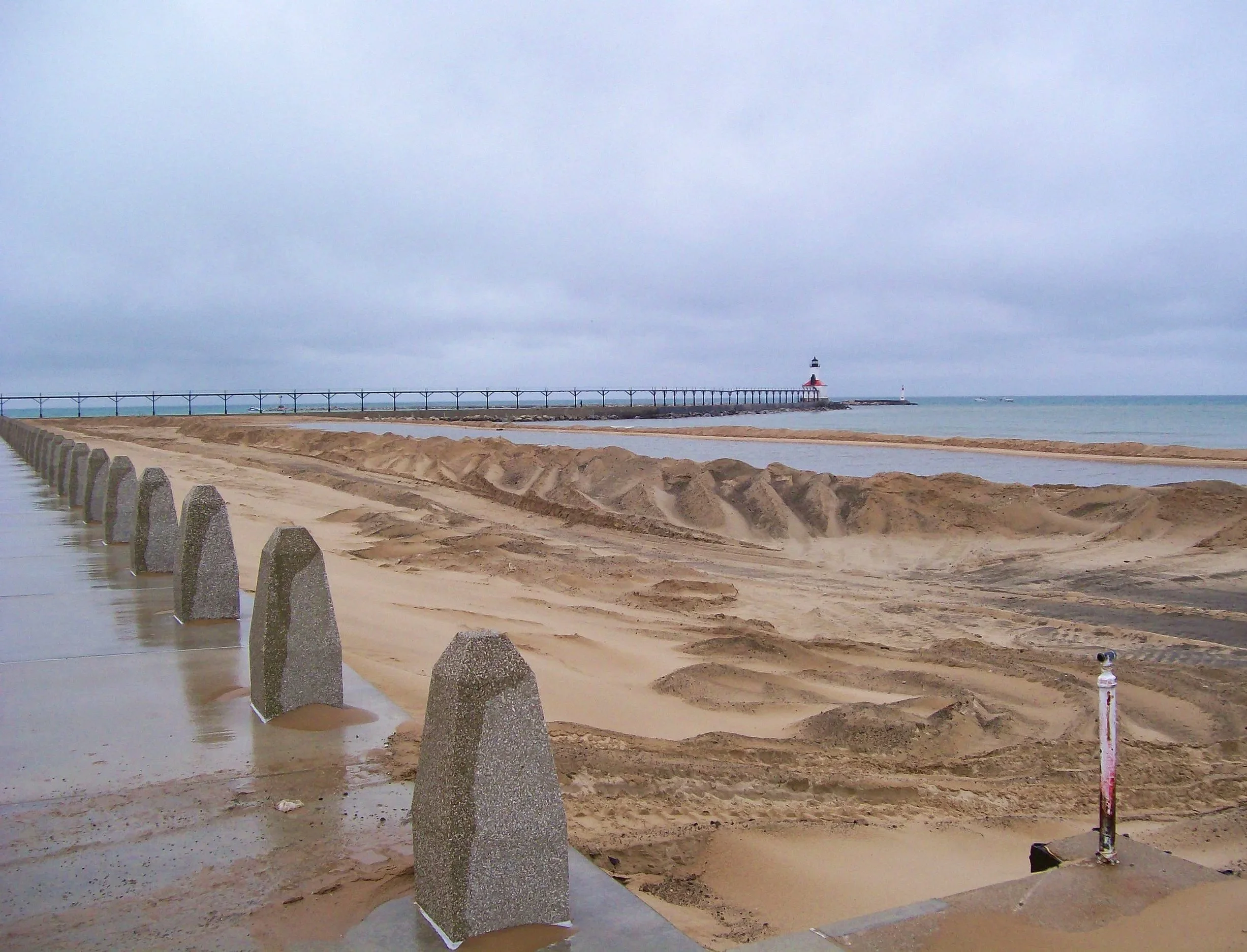 A boat cleaning or maintenance vessel on a harbor water with floating barriers and a marina with empty docks.