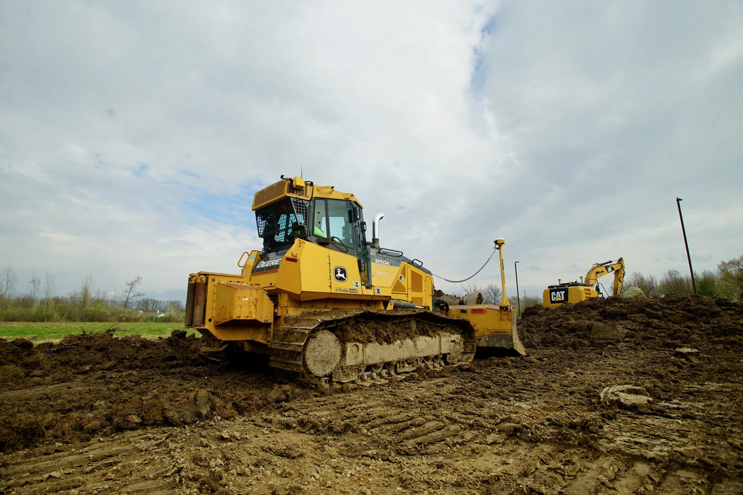 Construction site with a yellow bulldozer and a yellow excavator on dirt under a cloudy sky.