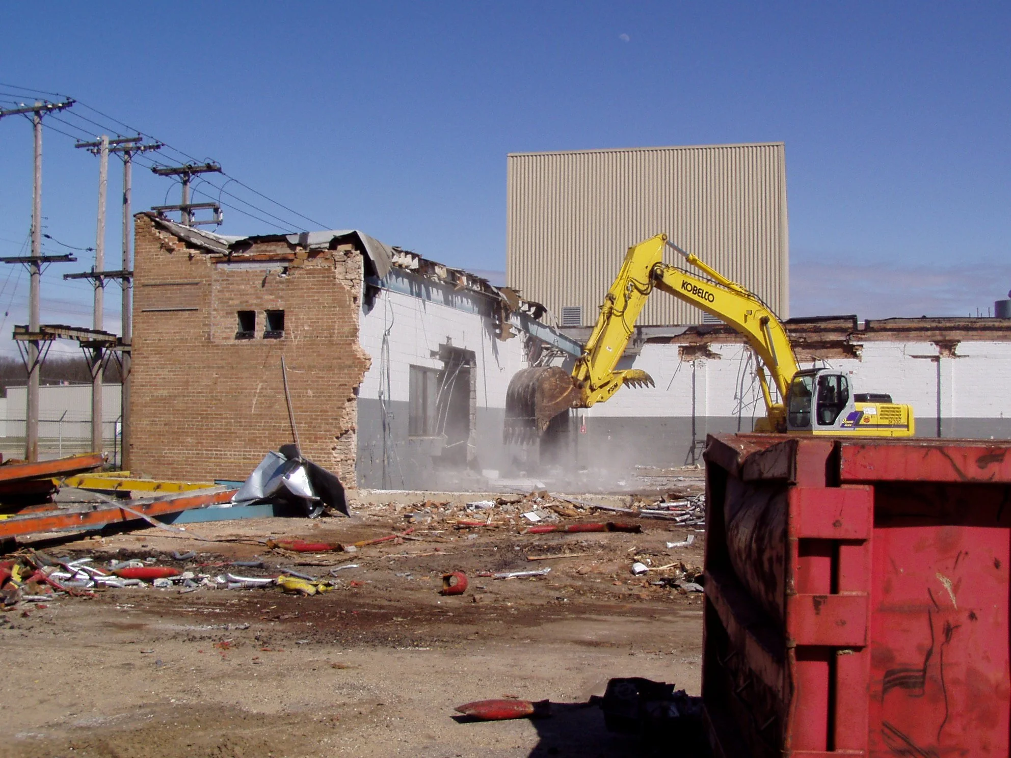 Construction demolition site with a yellow excavator tearing down a brick building on a clear day.