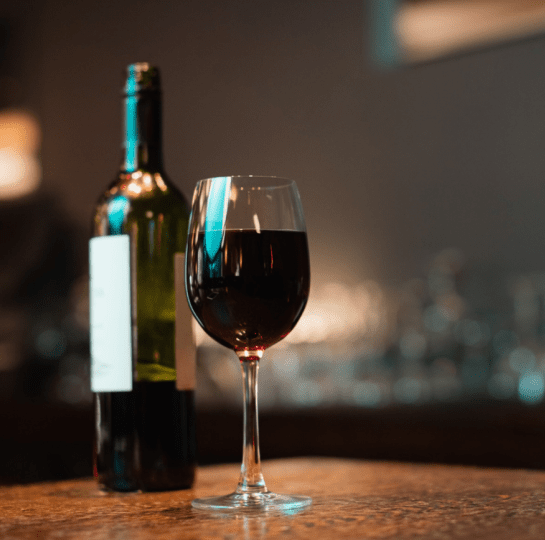 Glass of red wine and a wine bottle on a wooden surface in a dimly lit setting