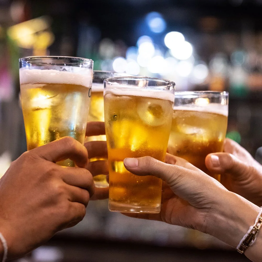 Three people clinking glasses of beer in a toast at a bar.