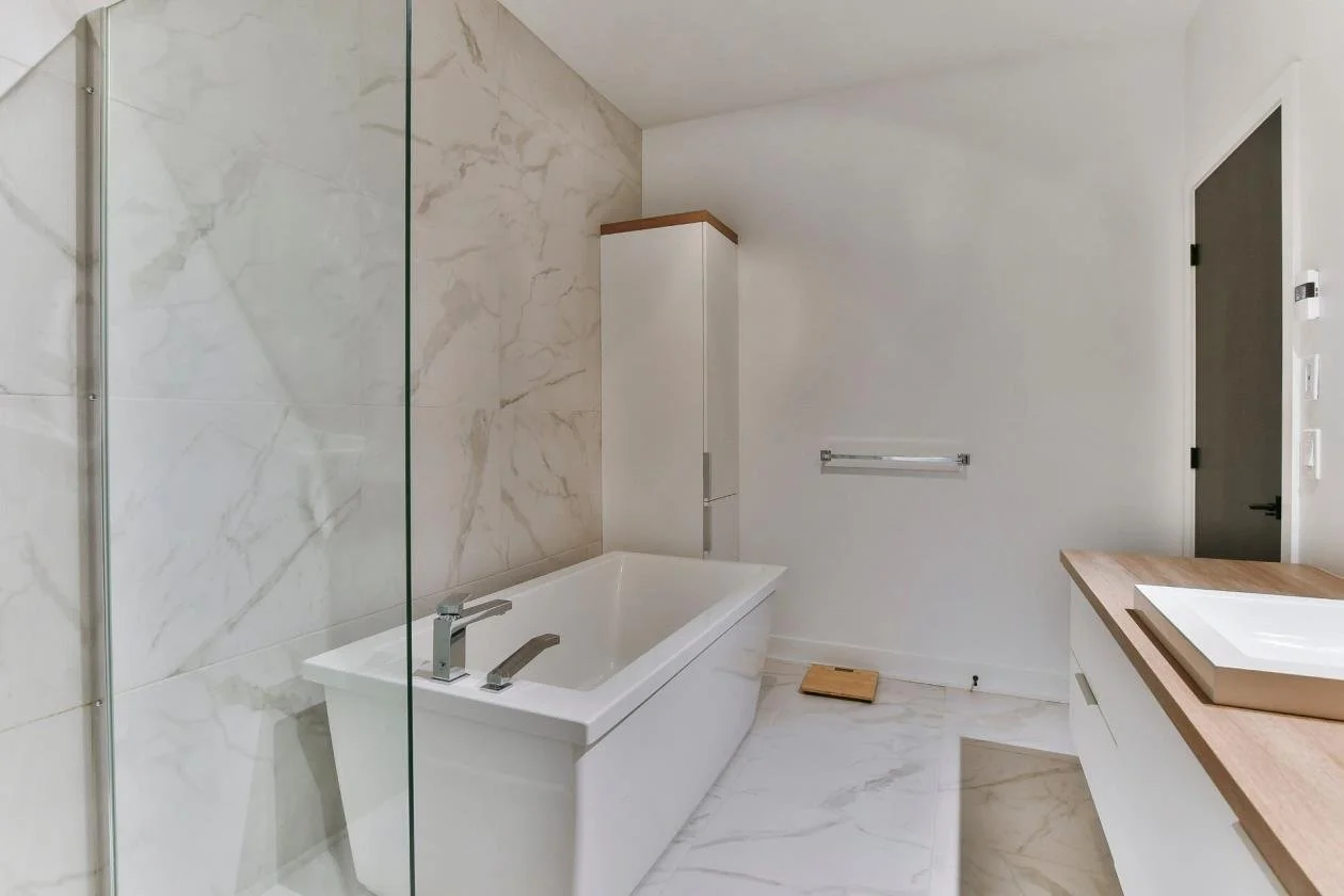 Salle de bain moderne avec baignoire, toilette, meuble avec lavabo en pierre et murs en marbre blanc.