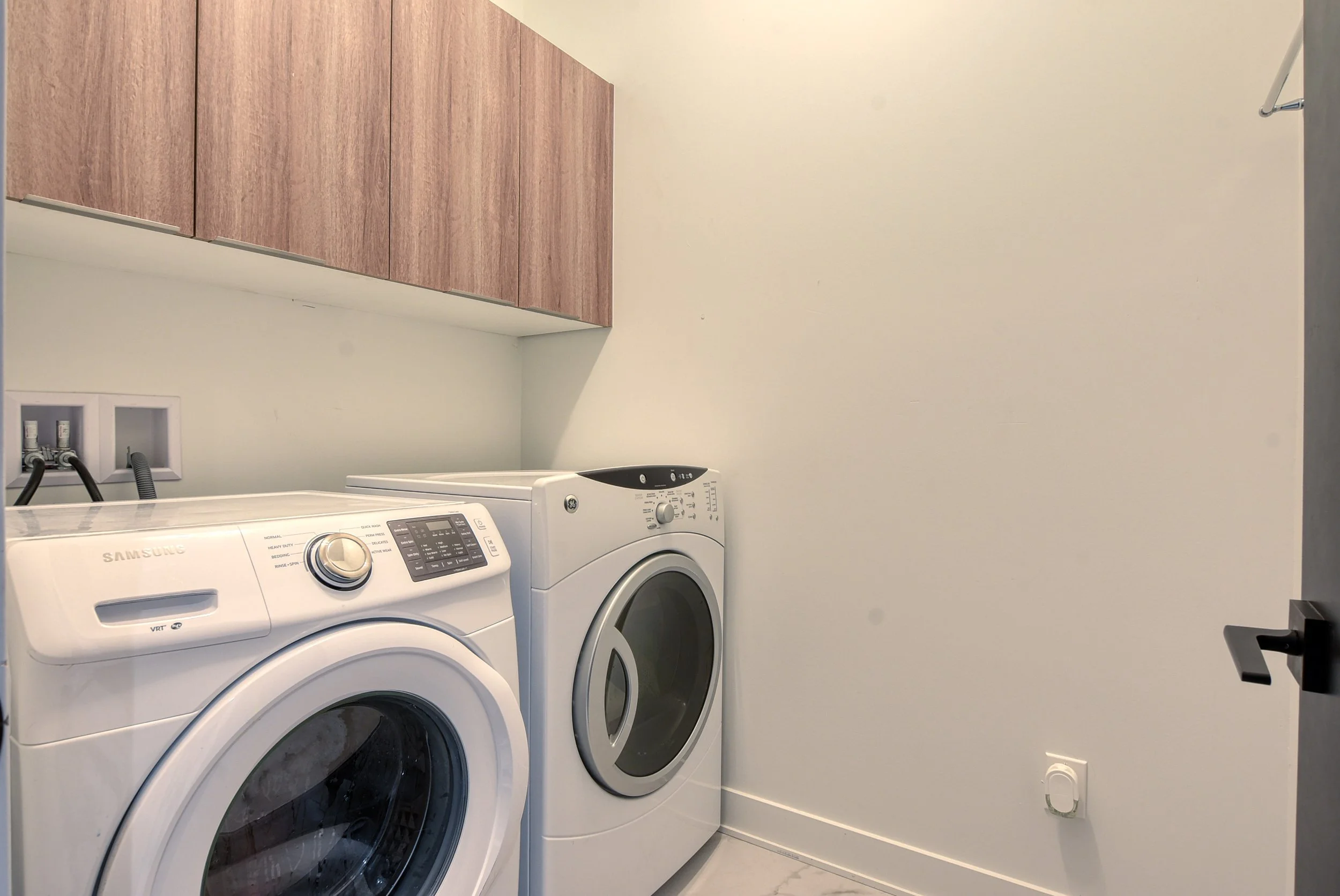 Lave-linge et sèche-linge blancs dans une buanderie avec placards en bois au mur