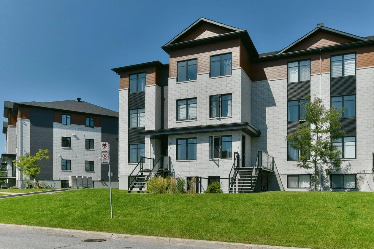 Appartement moderne avec plusieurs étages, escaliers extérieurs, grandes fenêtres, et un petit jardin en avant, dans un complexe résidentiel.