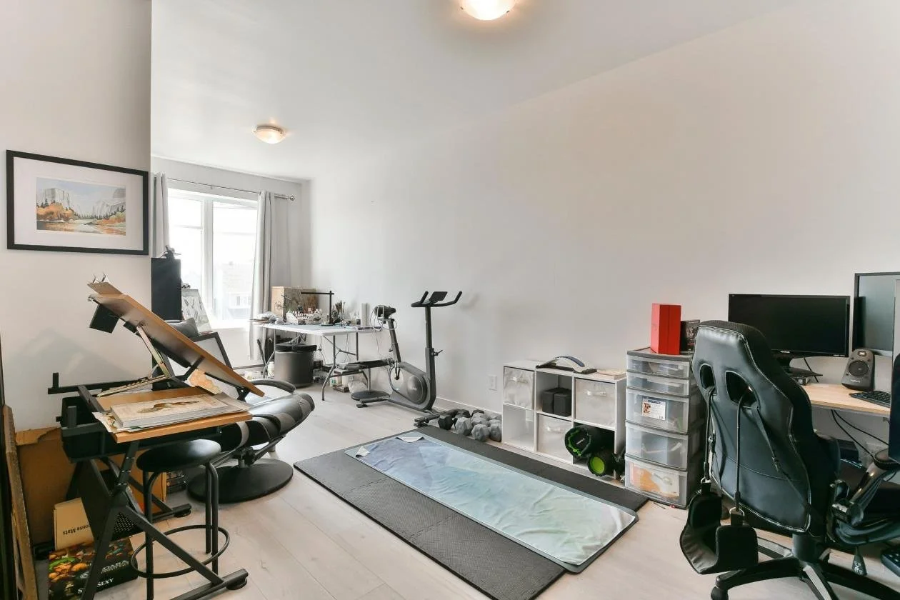 Une salle de sport à domicile avec équipement d'exercice, bureau avec ordinateur, et espace de travail.