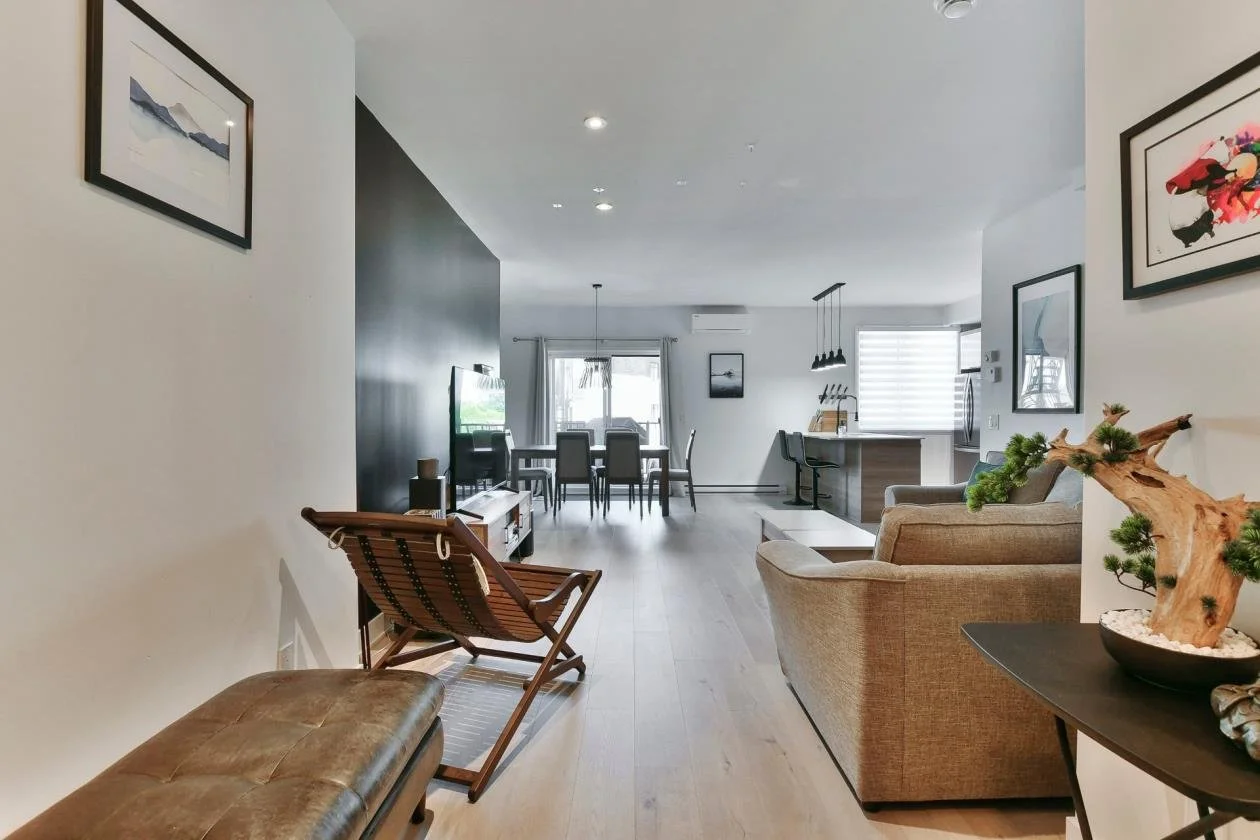 Salon moderne avec canapé beige, table basse, et décoration naturelle, ouvert sur une salle à manger et une cuisine.