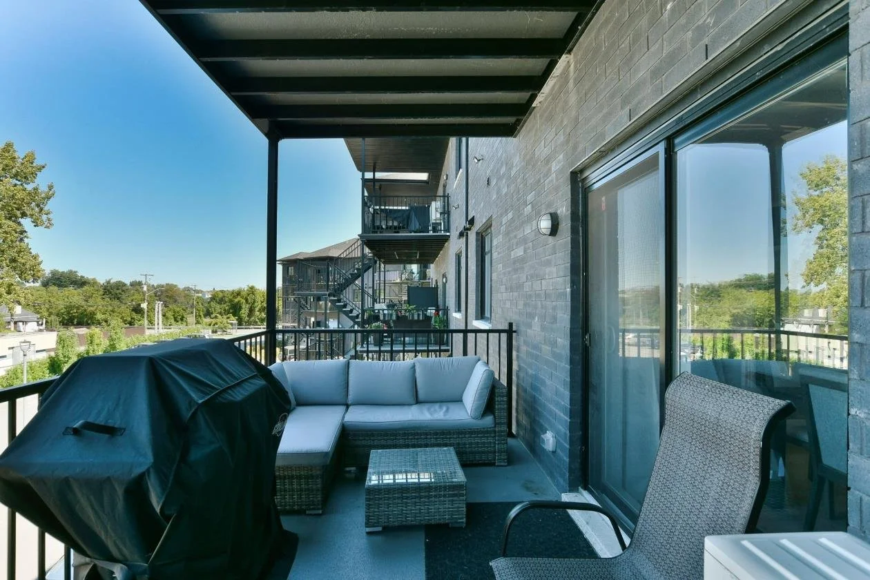 Balcon d'un appartement avec un canapé, une chaise, un barbecue, une table et une vue sur la ville.
