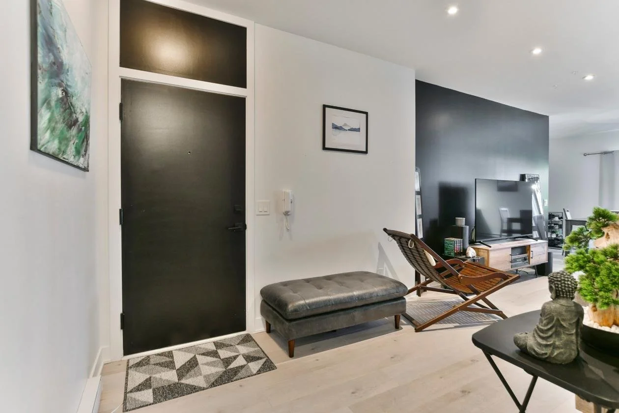 Entrée d'un appartement avec porte noire, petit tapis sur le sol, fauteuil en bois, télévision et décoration intérieure moderne.