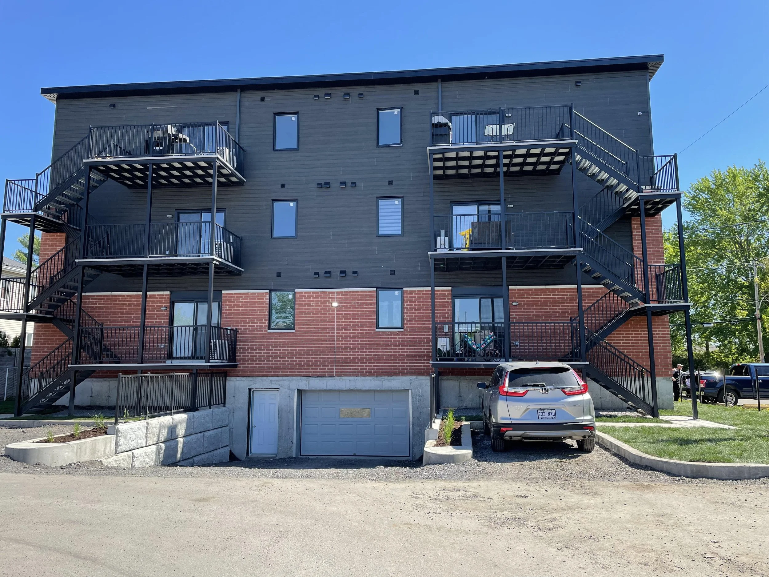 Immeuble résidentiel à trois étages avec escaliers extérieurs en métal et parking en sous-sol, façade en brique rouge et revêtement noir