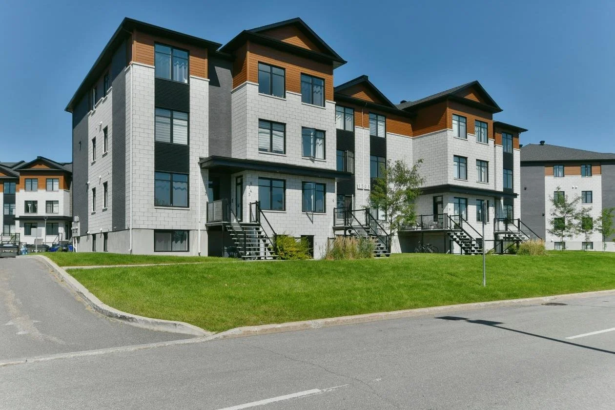 Maisons individuelles modernes avec escaliers devant, pelouse verte et arbres dans un quartier résidentiel.
