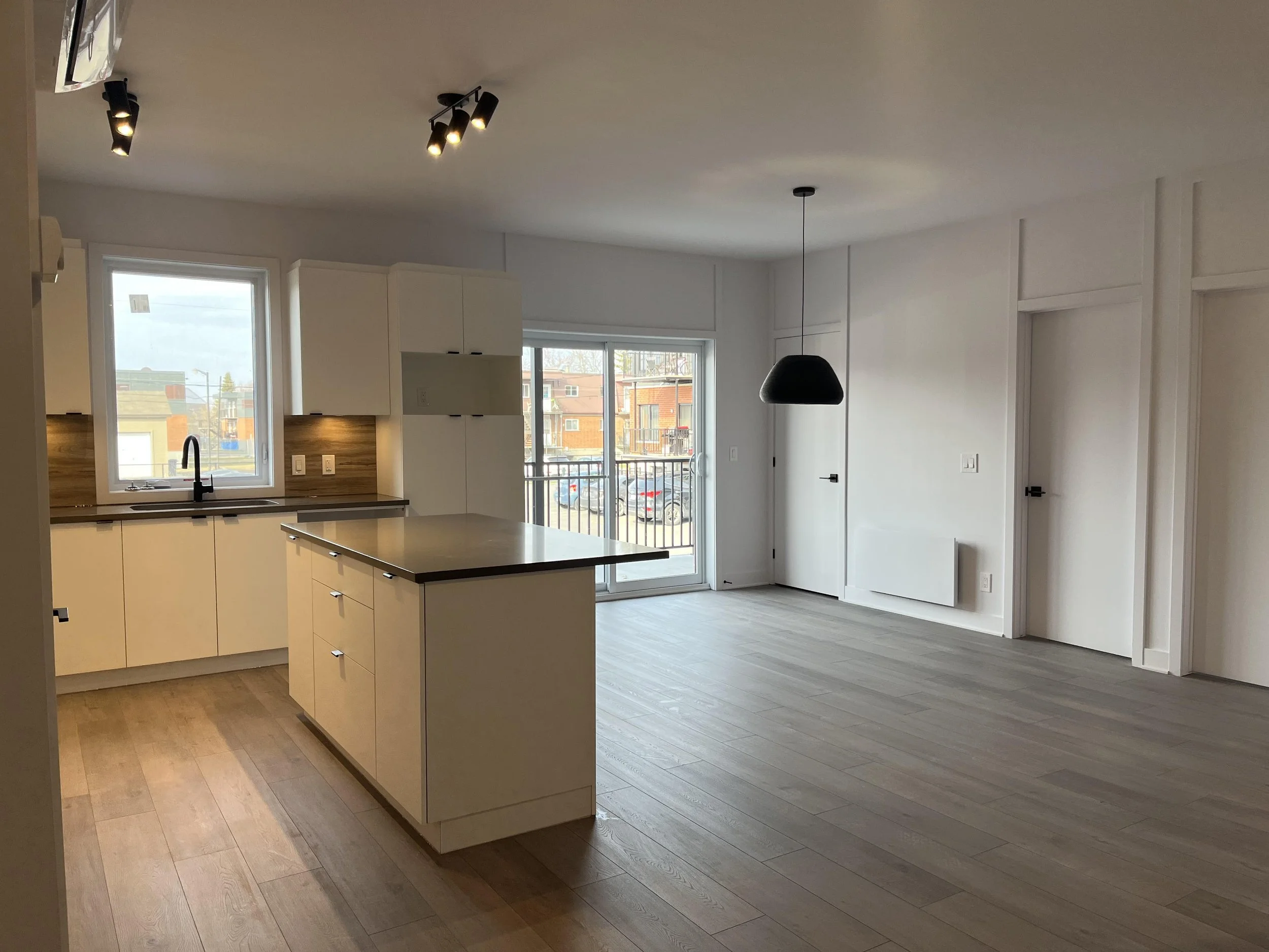 Cuisine moderne avec comptoir, évier sous la fenêtre, et espace ouvert avec sol en bois clair