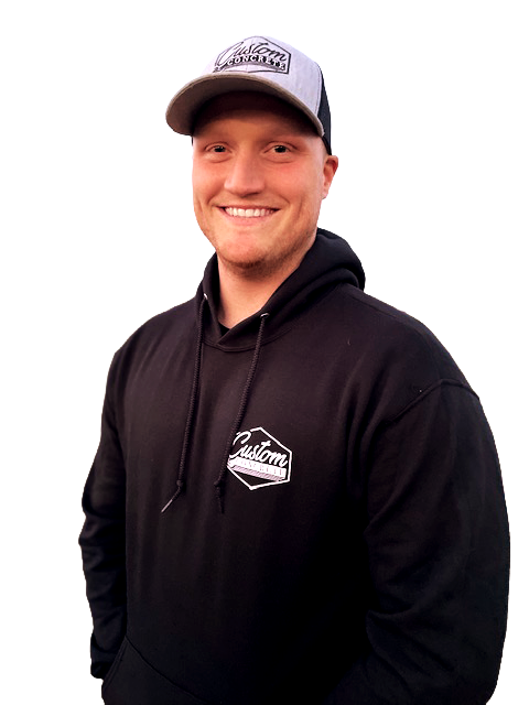 Smiling young man wearing a gray and black baseball cap and black hoodie with a logo, standing against a plain background.