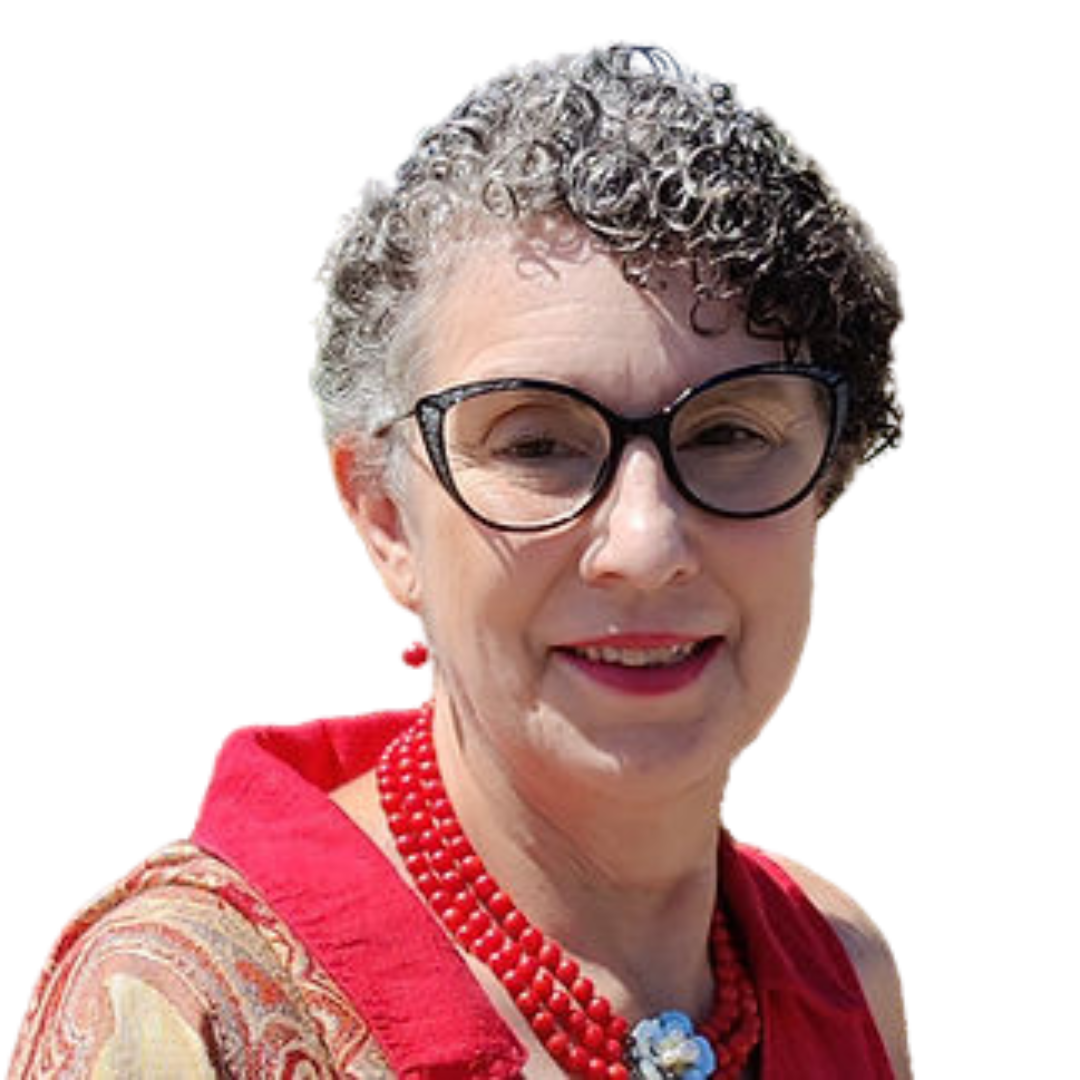 Close-up of a smiling woman with short curly gray hair, black glasses, red lipstick, red beaded necklace, and red earrings, wearing a patterned top.