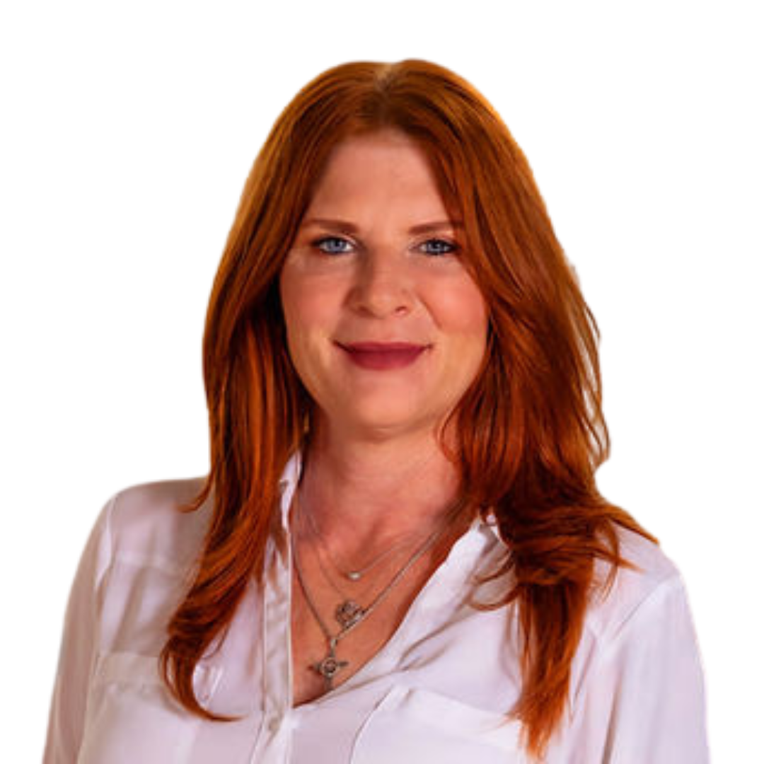 Portrait of a woman with red hair, blue eyes, wearing a white blouse and layered necklaces, smiling at the camera.