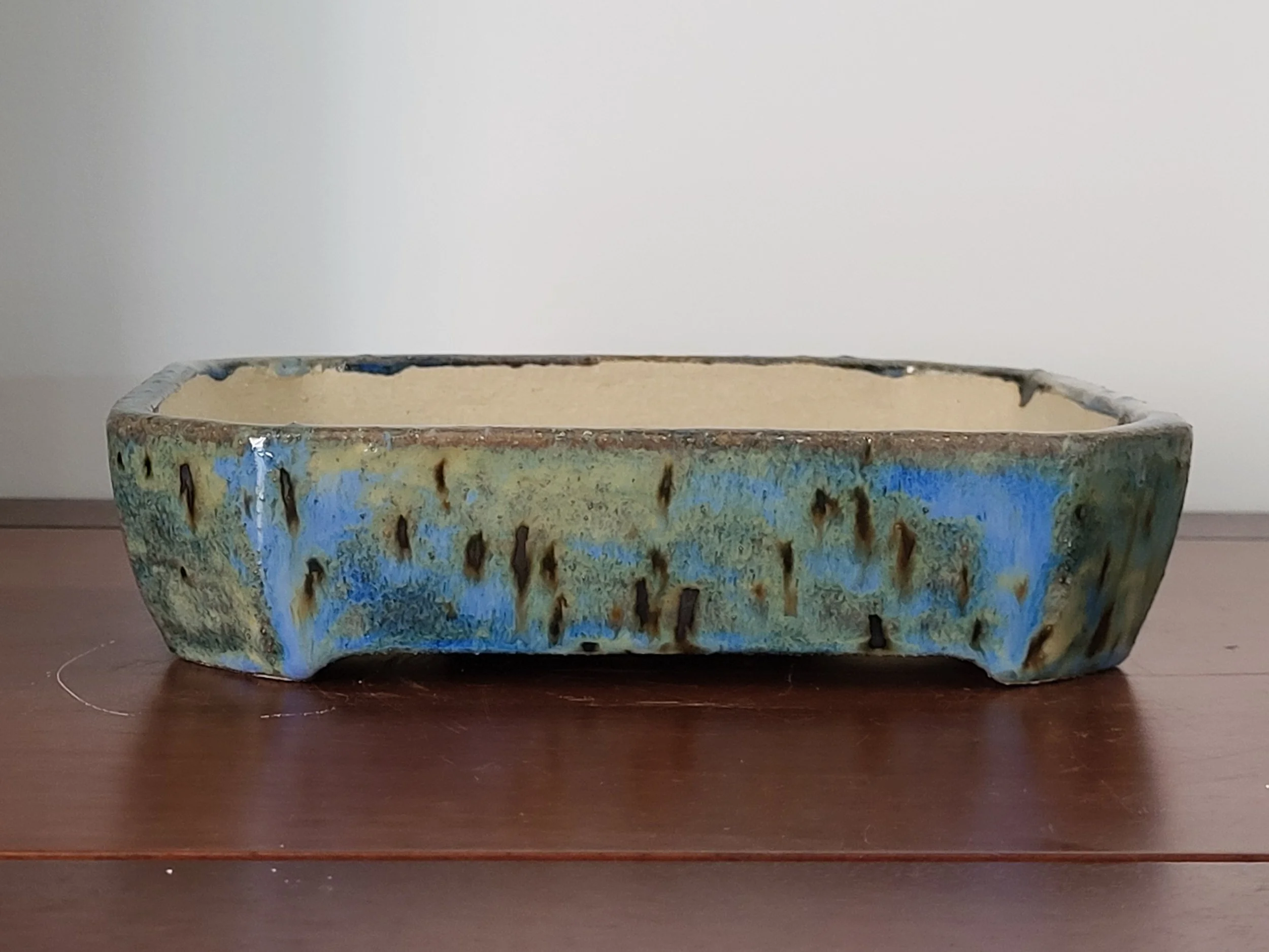 A rectangular ceramic planter with a textured glaze finish in blue, green, and beige tones, sitting on a wooden surface.