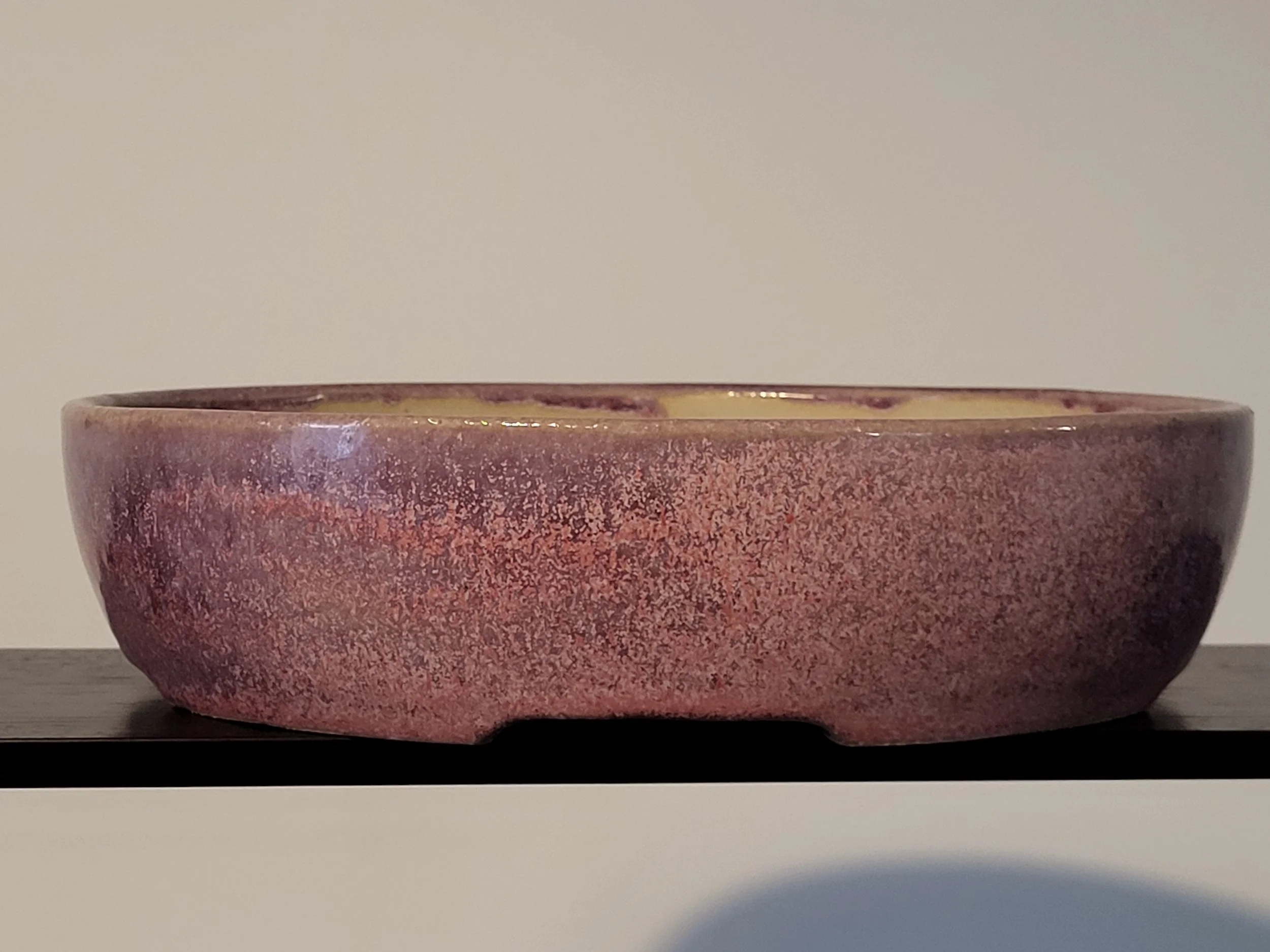 A pink ceramic bowl with a smooth textured surface on a black shelf against a plain background.
