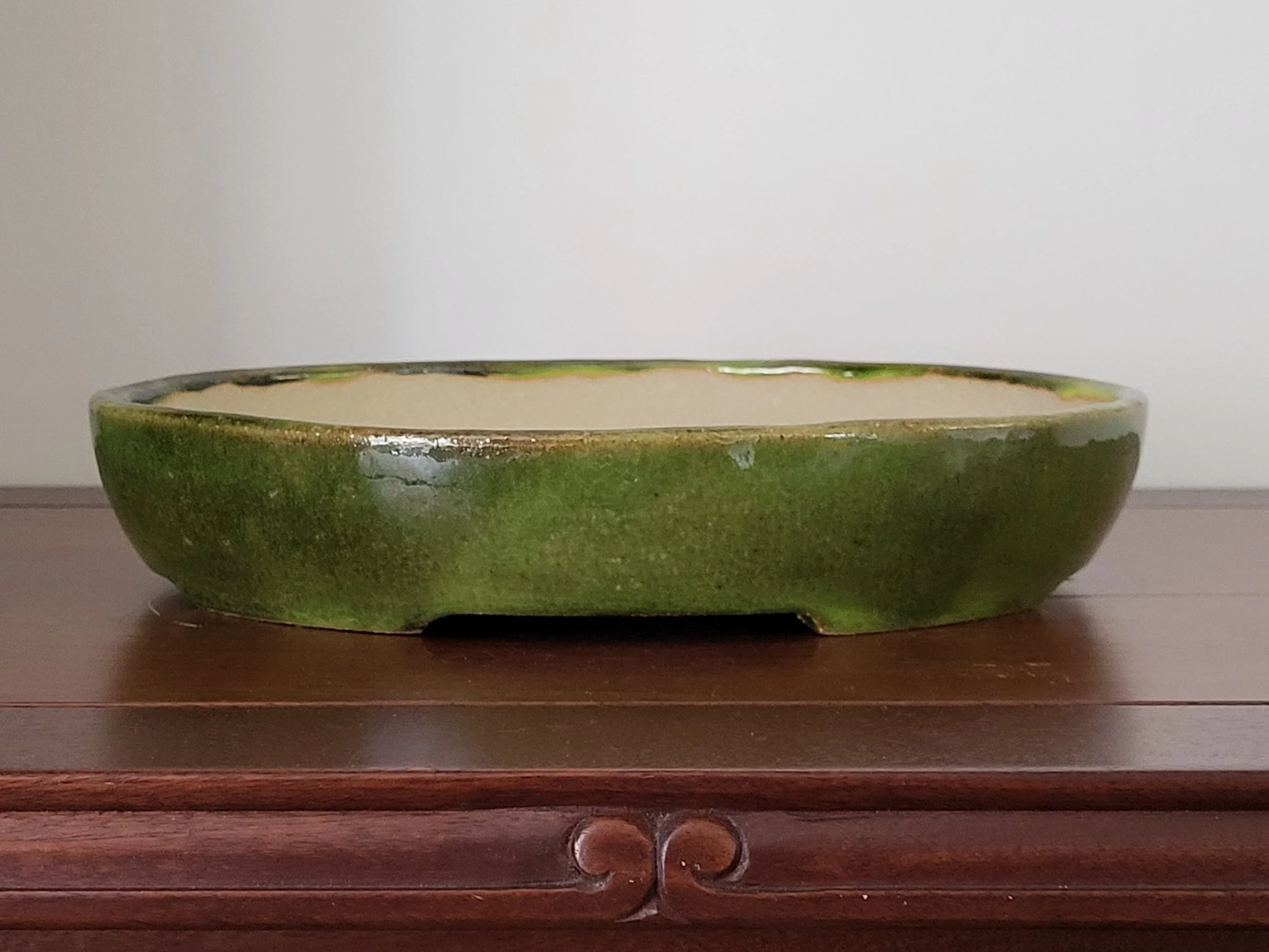 A shallow ceramic bowl with a green glaze on the outside and a white interior, placed on a wooden surface against a plain wall background.